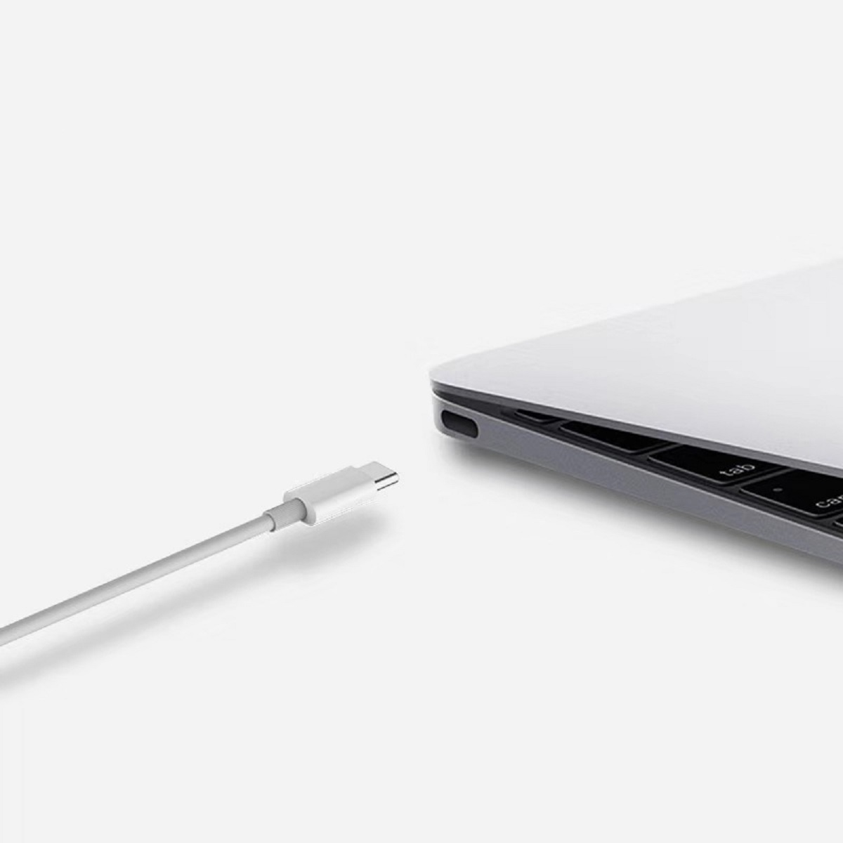 Ein weißes USB-C-Kabel liegt neben einem silbernen Laptop.