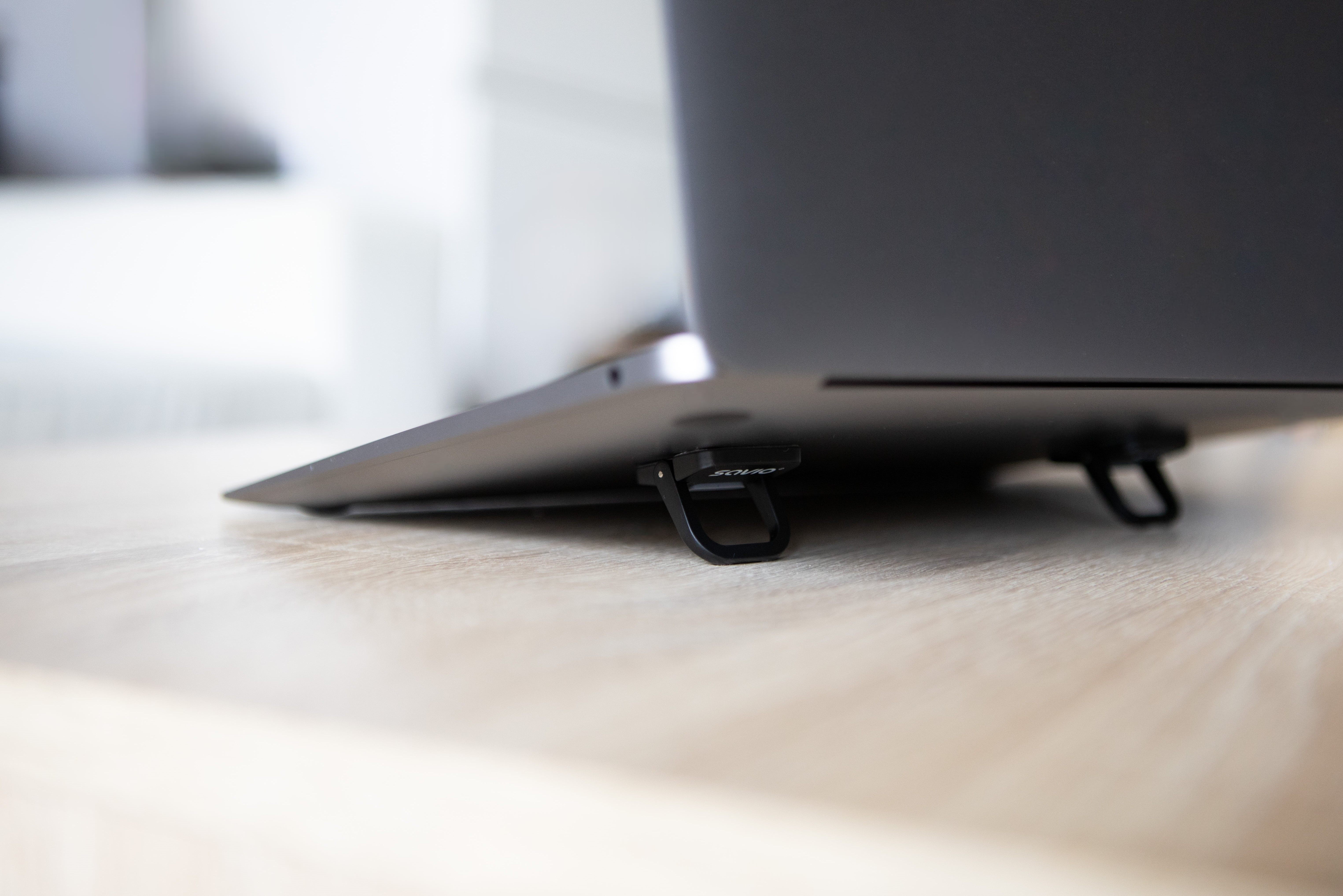 A laptop sits on a wooden desk, its feet are foldable.