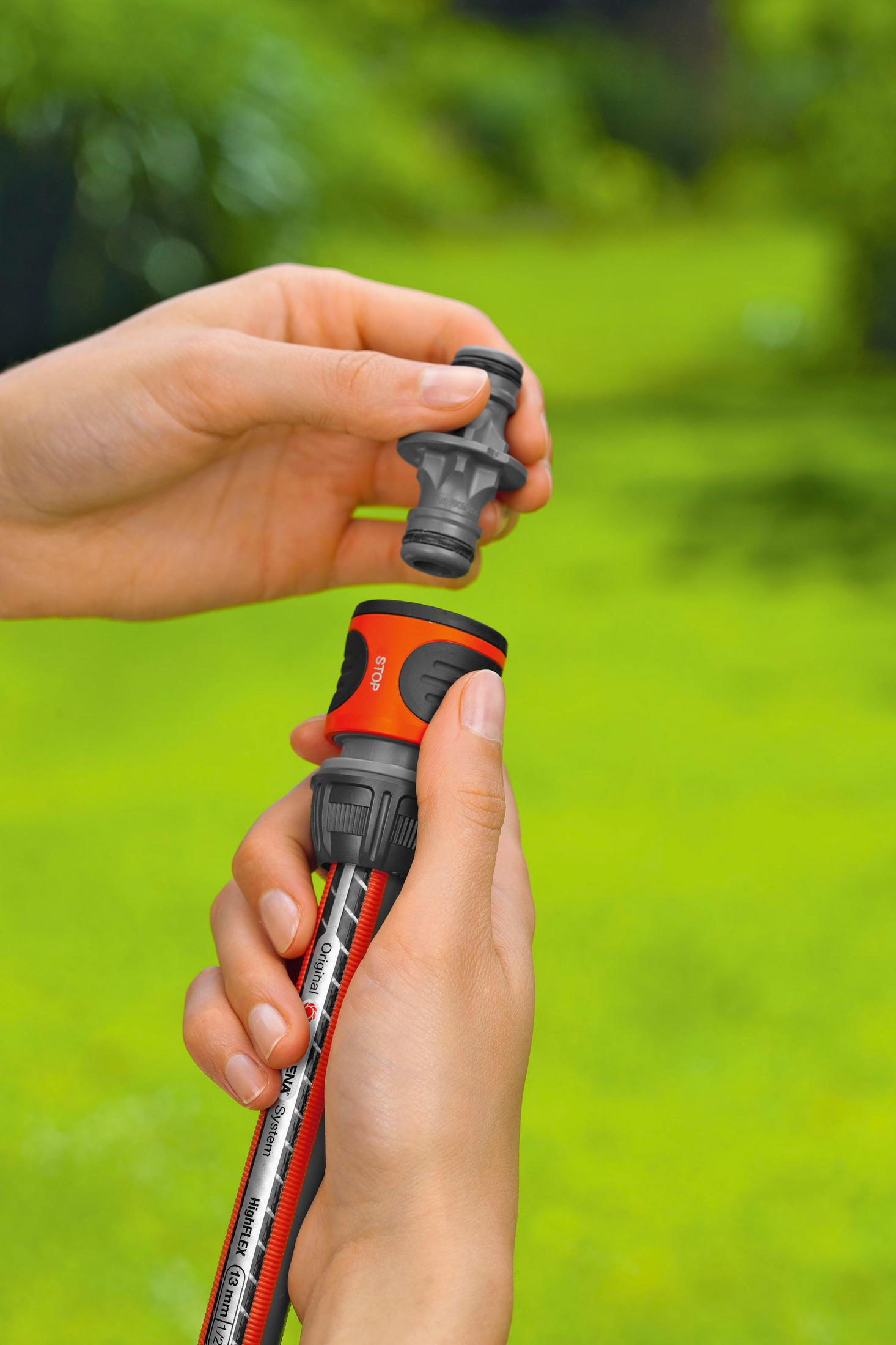 Mani che collegano un tubo da giardino con manico arancione e pulsante stop.