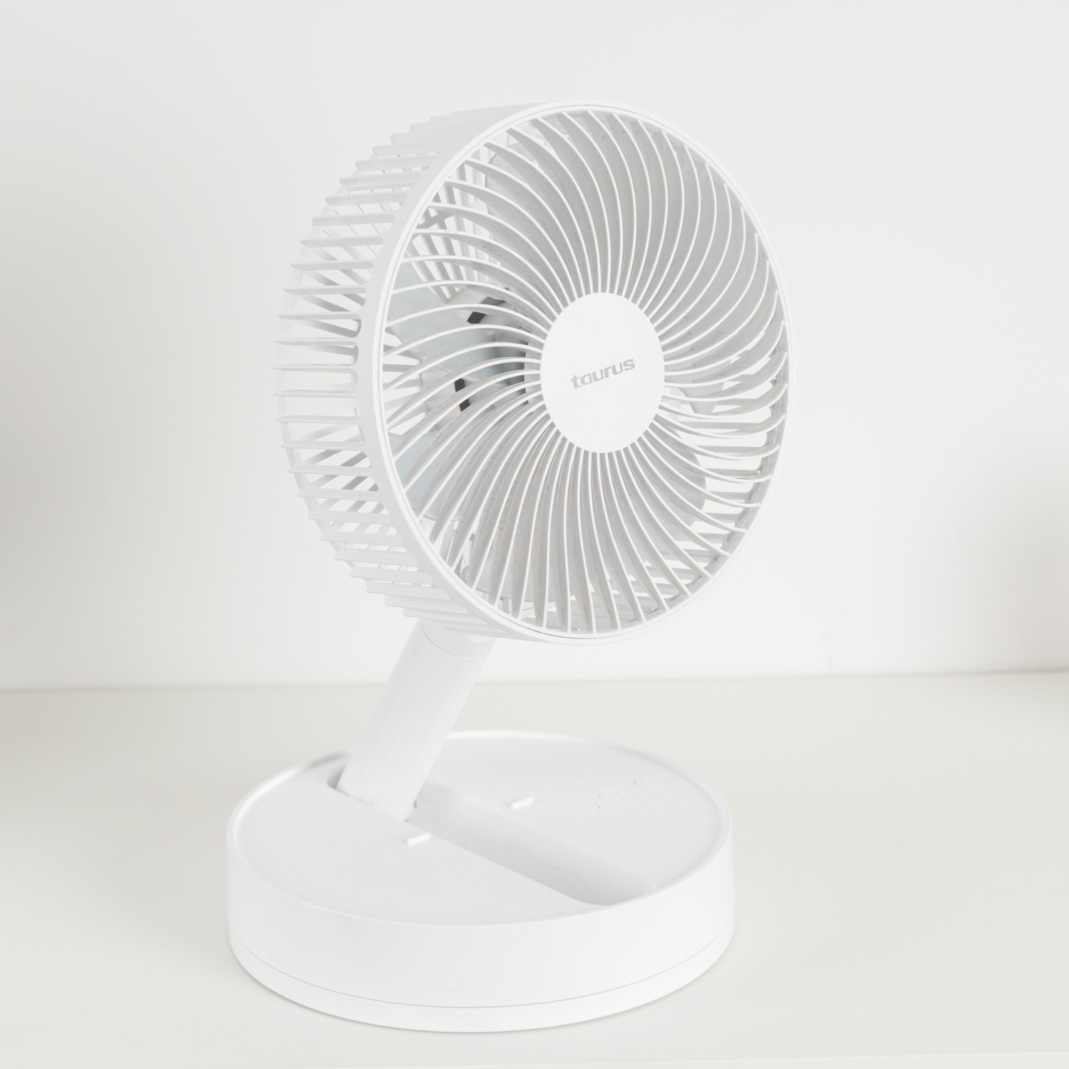 Un ventilador de escritorio blanco marca Taurus con rejilla redonda sobre una superficie blanca.