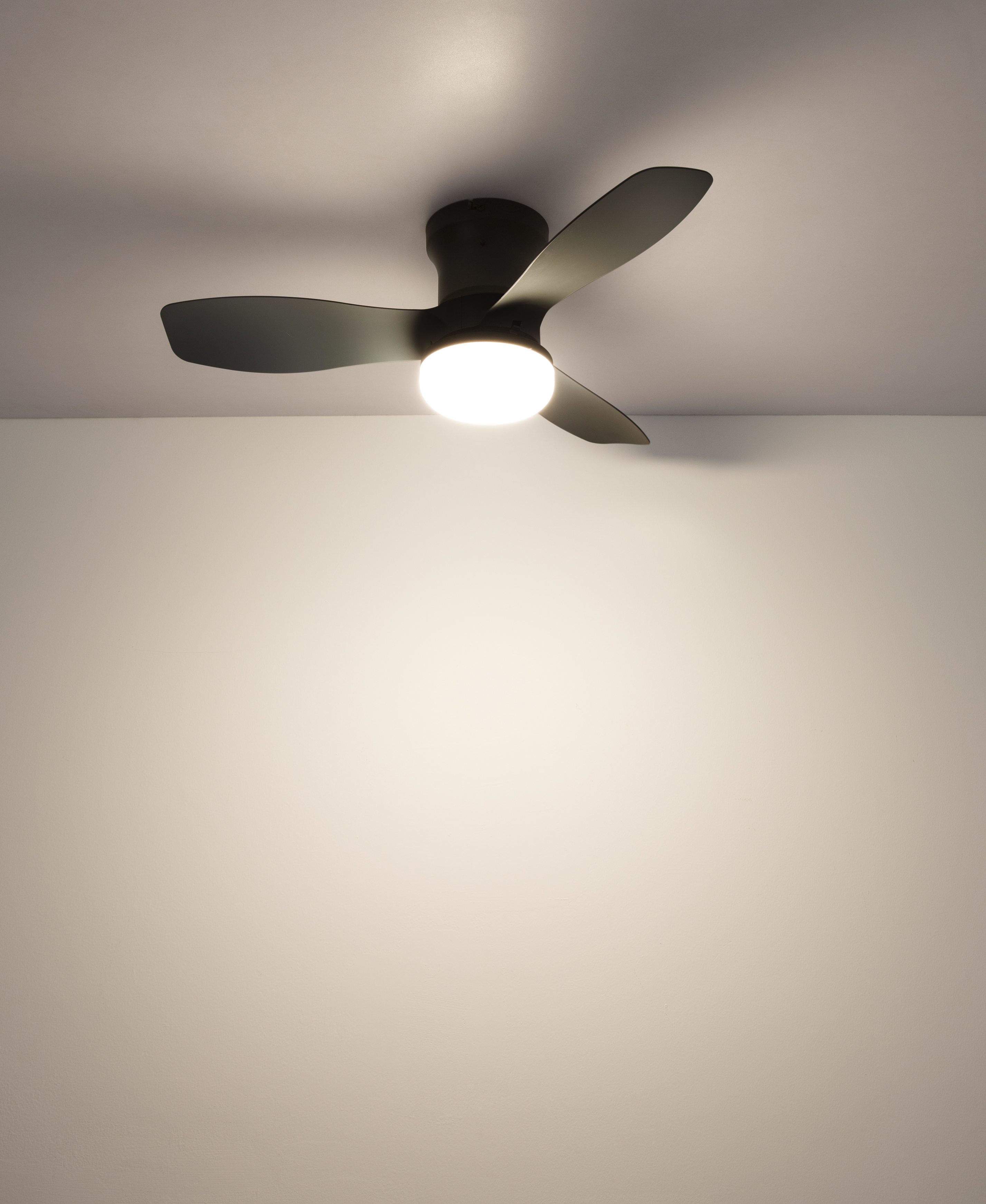 Ein dunkler Deckenventilator mit drei Flügeln und einer beleuchteten Mitte, montiert an einer weißen Decke.