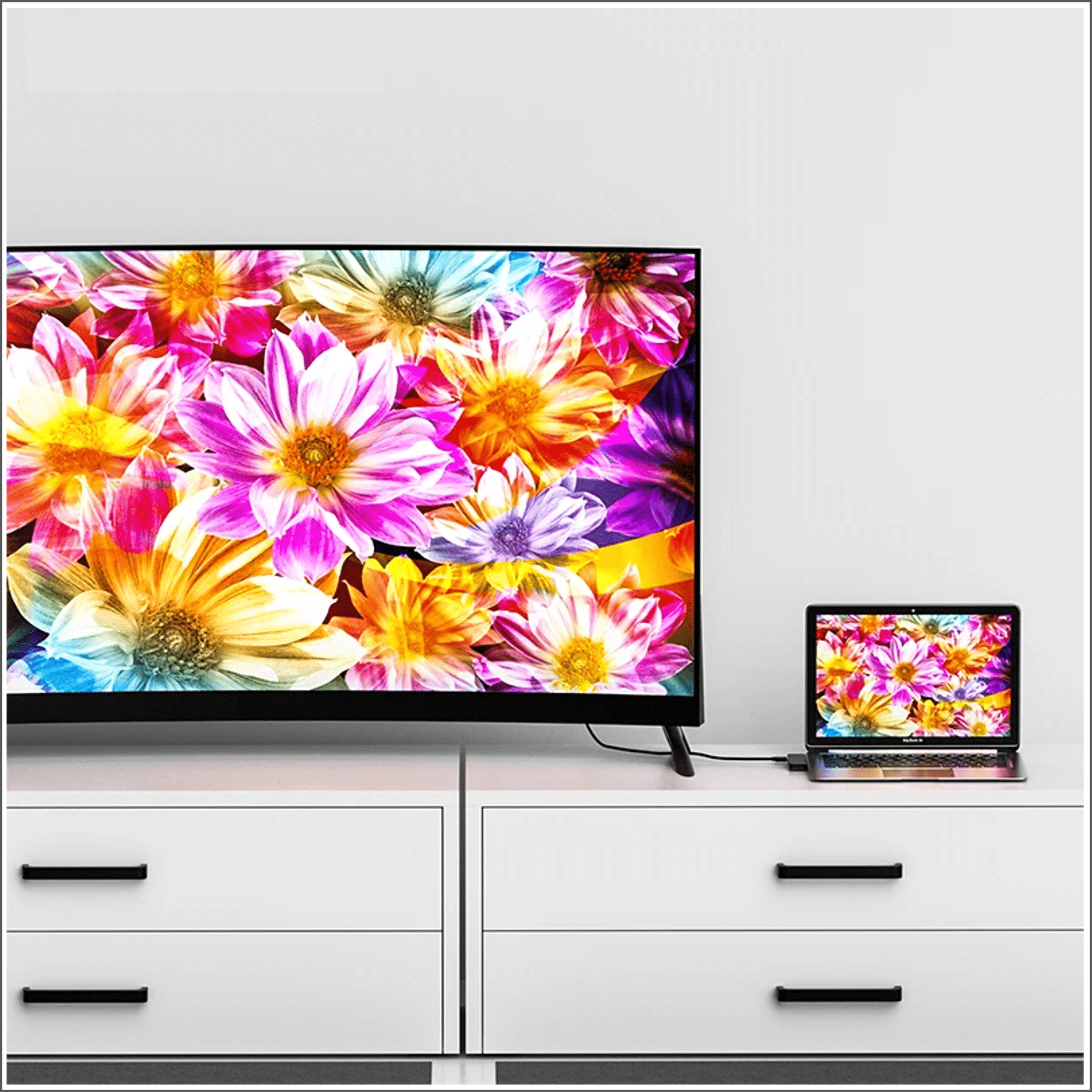 A large TV and laptop display colorful flower images on a white cabinet.