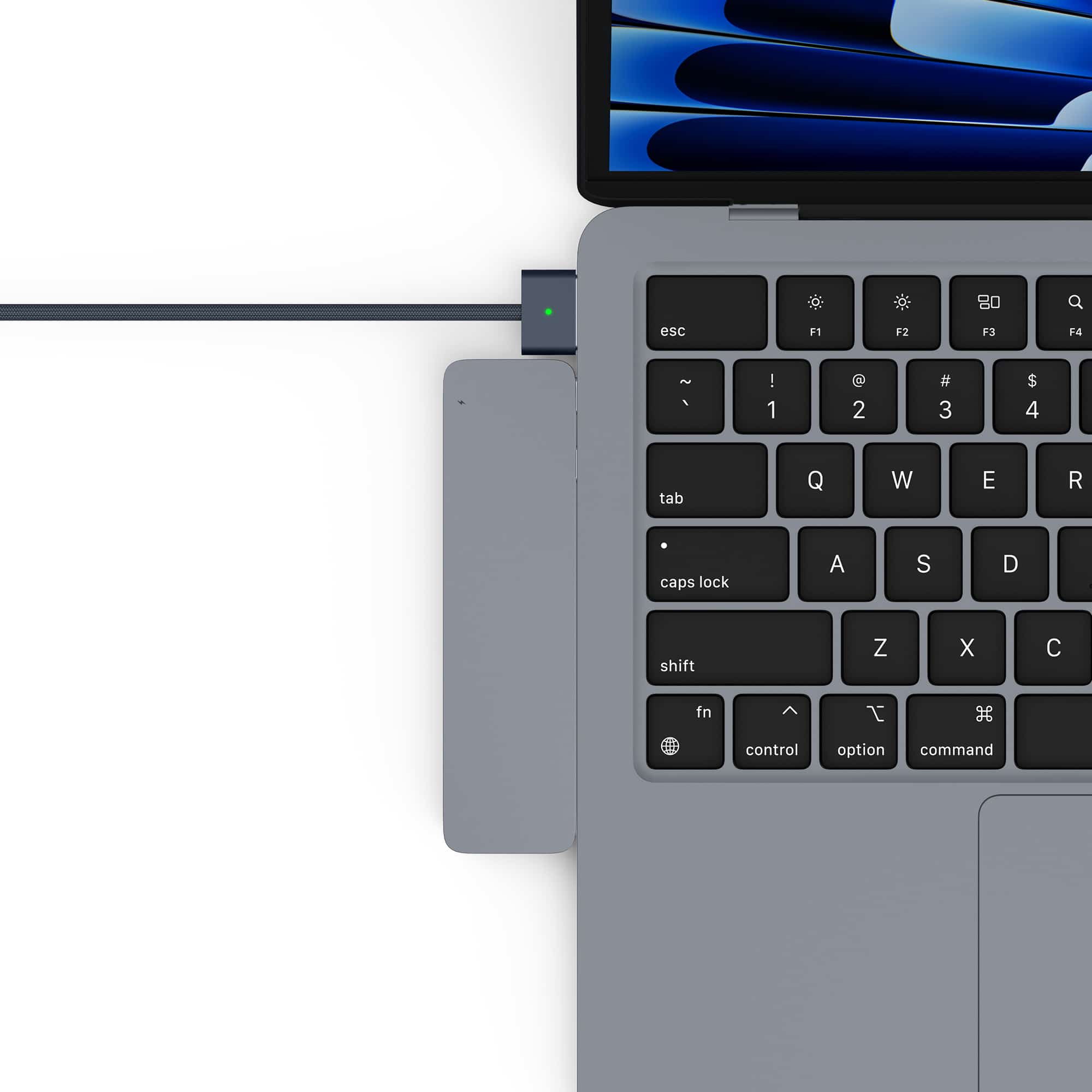 A gray USB-C hub is connected to a MacBook, with a green indicator light.