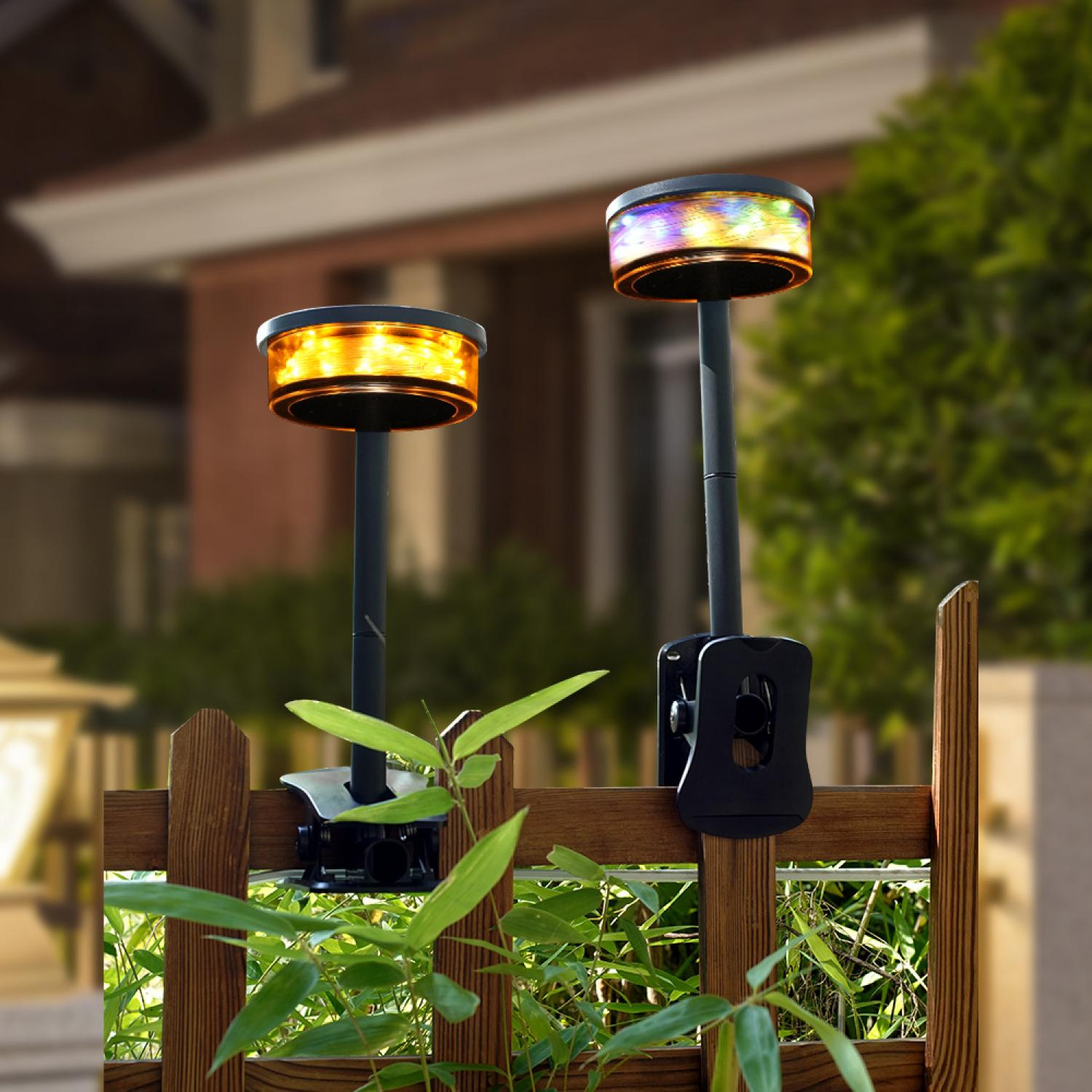 Zwei Solar-Zaunlichter mit orangen und bunten LEDs sind an einem Holzzaun befestigt.