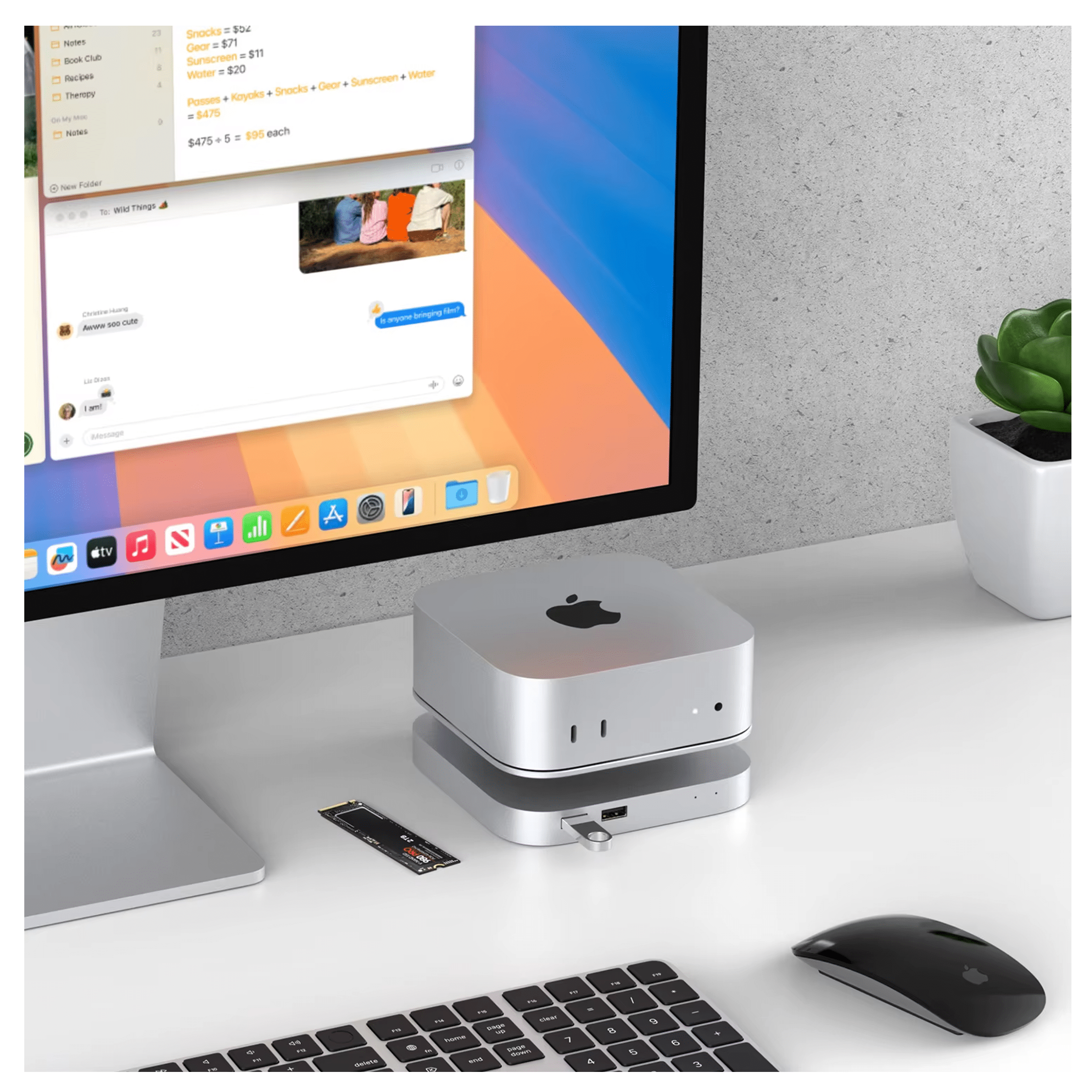 A silver Apple Mac Mini sits on a desk next to a keyboard, mouse, and SSD.