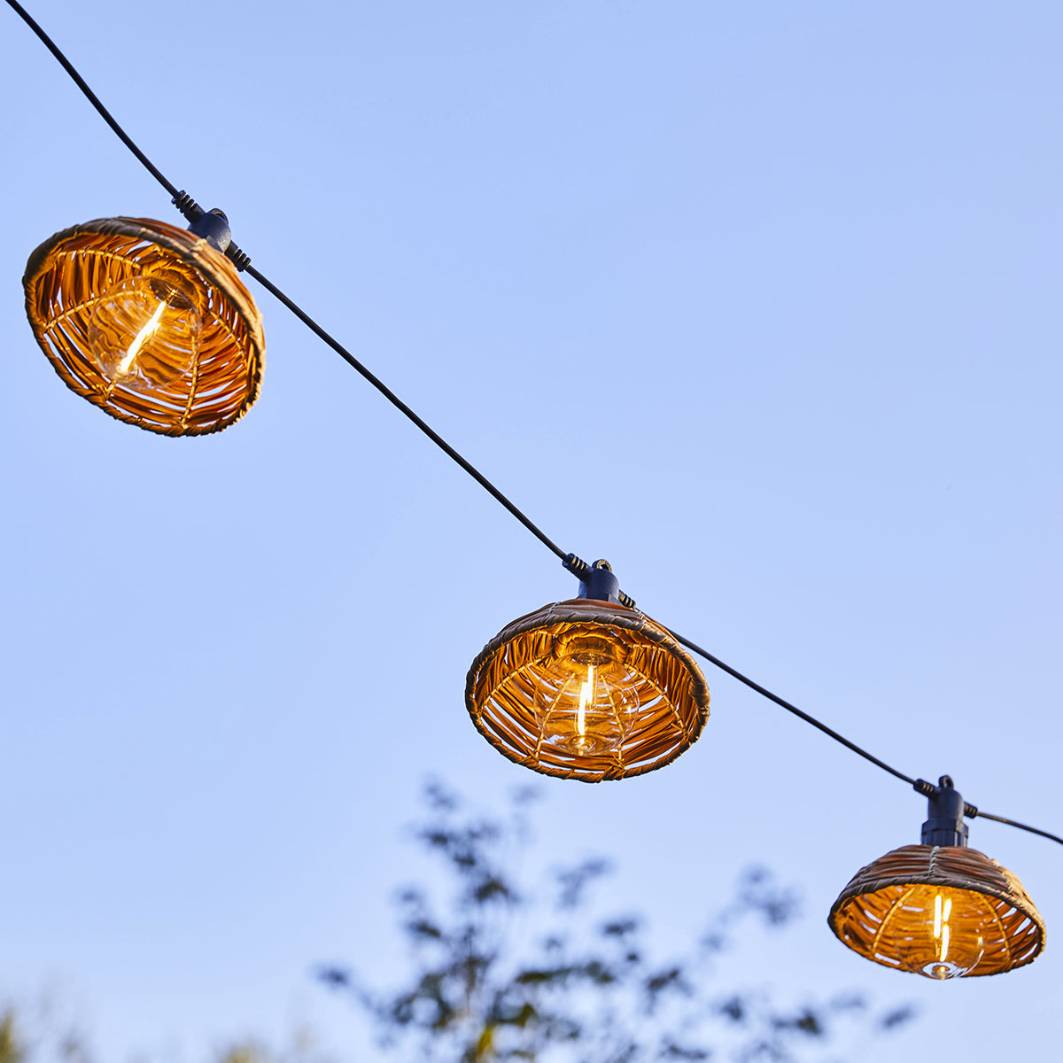 Drei geflochtene Lampenschirme an einem Kabel hängen im blauen Himmel.