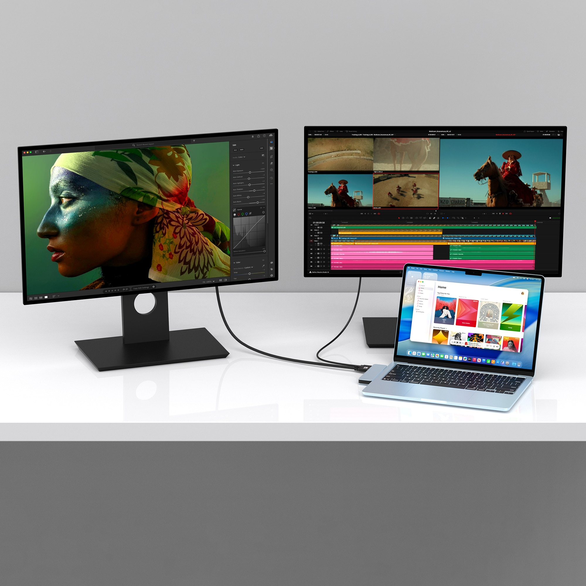 A laptop and two monitors display editing software. One shows a colorful face, the other a video timeline.