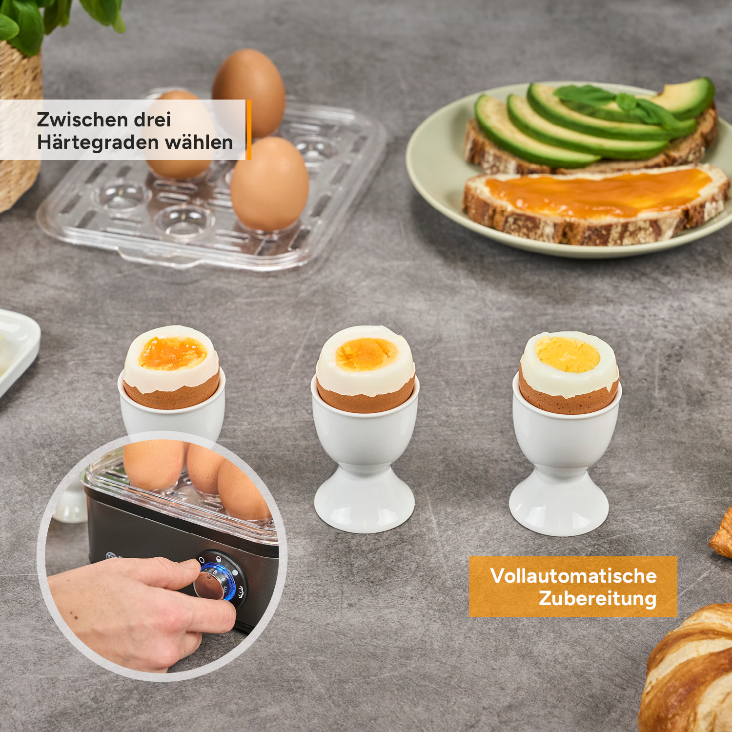 Drei gekochte Eier in Bechern, ein Eierkocher mit Hand, Toast mit Avocado und Marmelade.