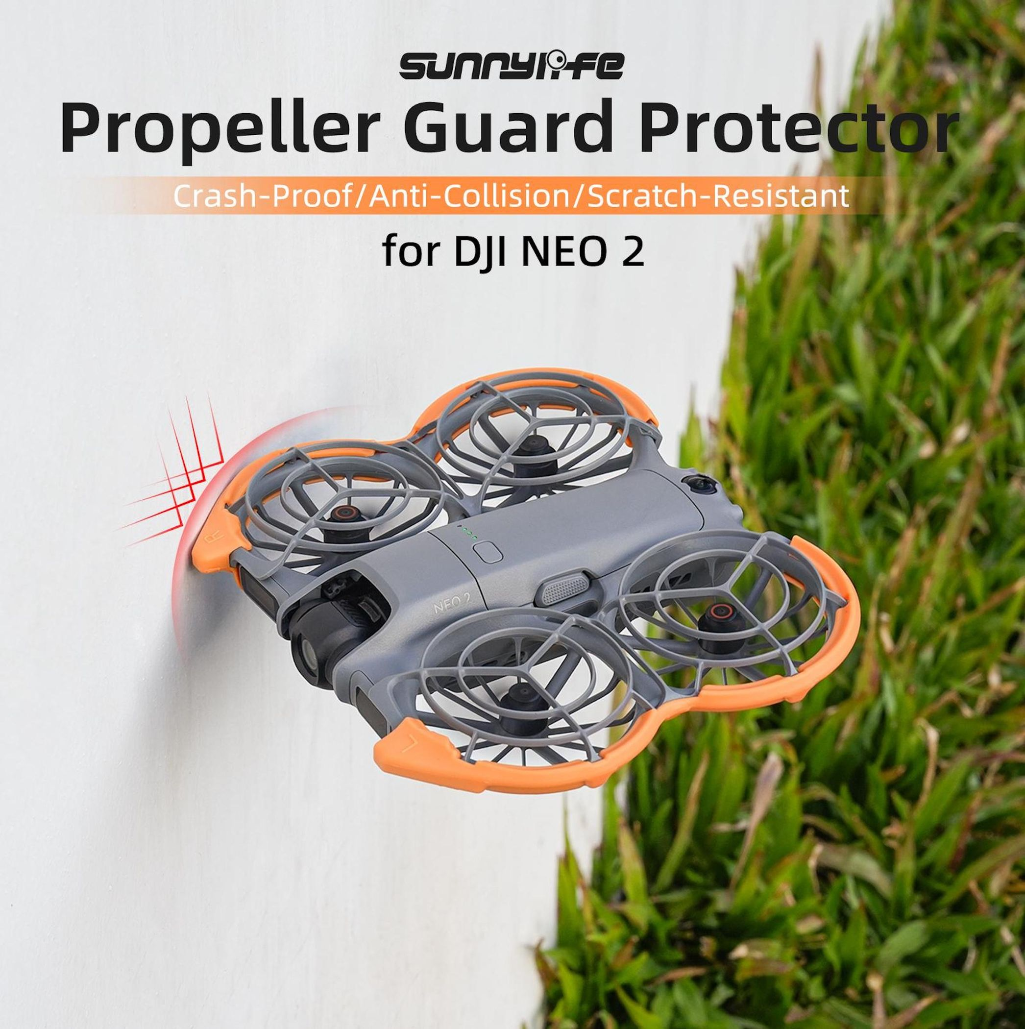 Graue Drohne mit orangem Propellerschutz vor einer weißen Wand und Gras.