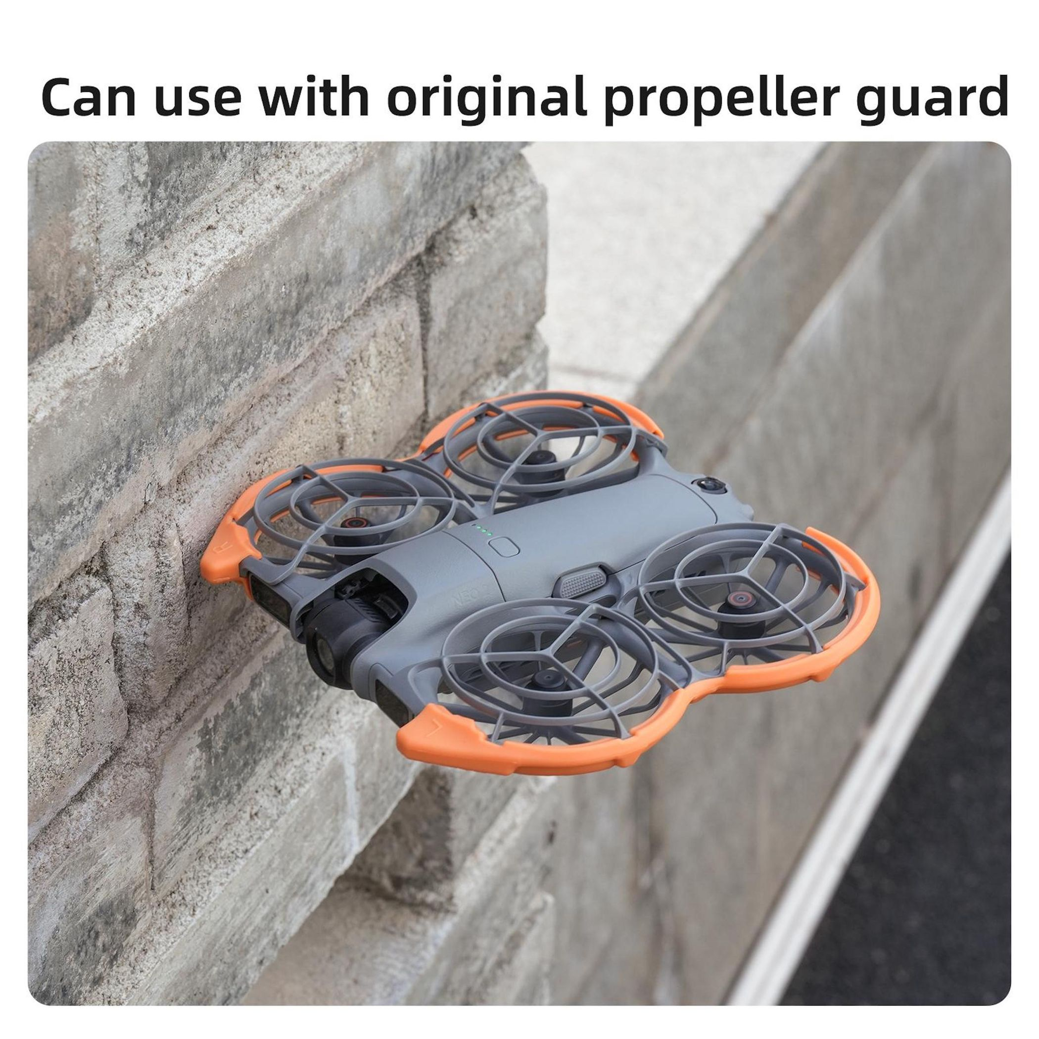 Grauer Mini-Quadrocopter mit orangefarbenen Propellerschützern, der an einer Steinwand hängt.