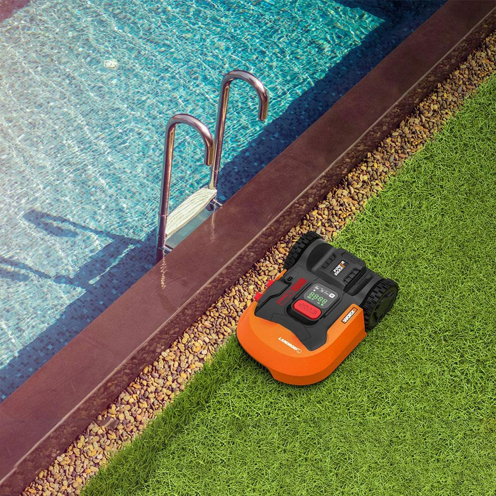 Ein Mähroboter auf dem Rasen neben einem Pool mit silbernen Leitern.