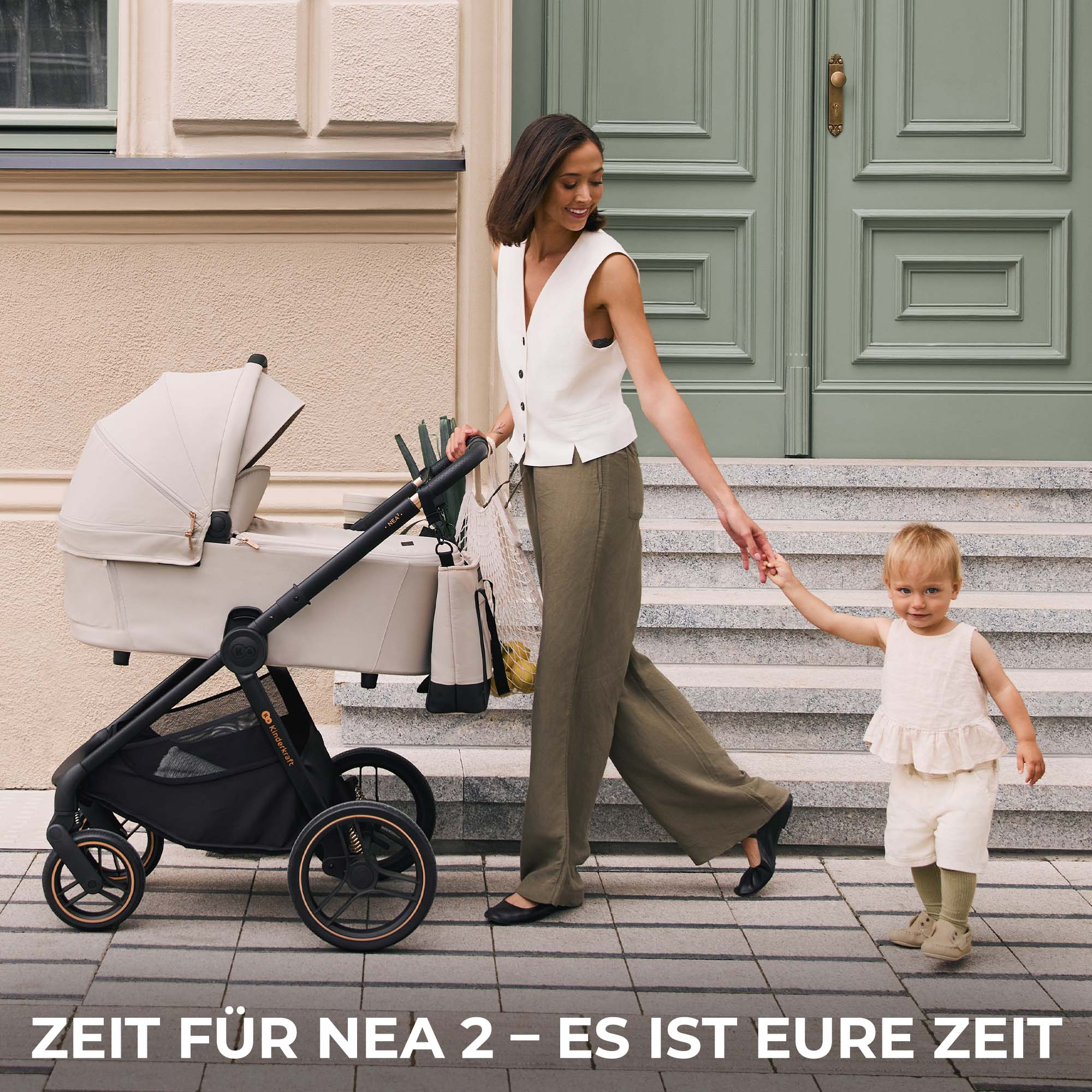 Eine Frau schiebt einen Kinderwagen und hält ein Kleinkind an der Hand vor einem Haus.