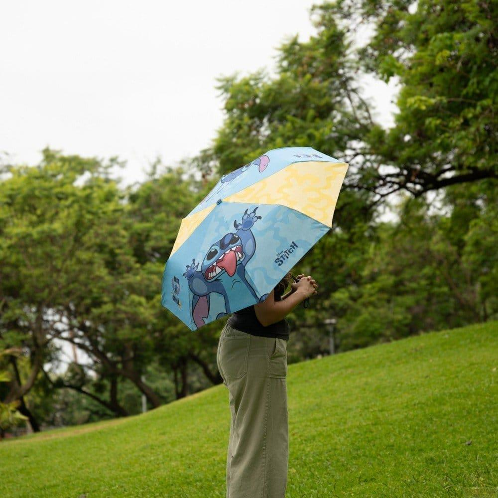 Persona sosteniendo un paraguas azul con diseño de Stitch al aire libre.