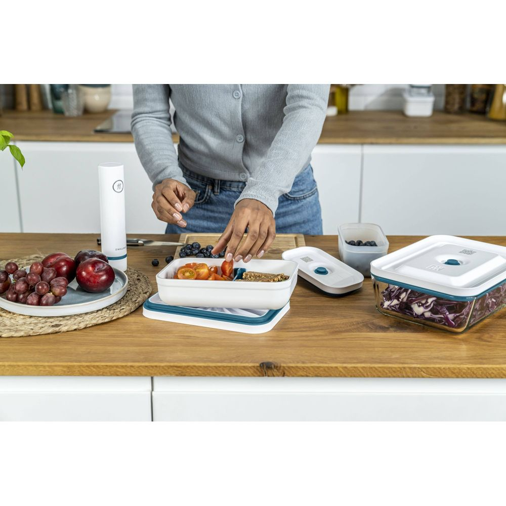 Una persona prepara cibo in contenitori. Frutta e verdura sono disposti.