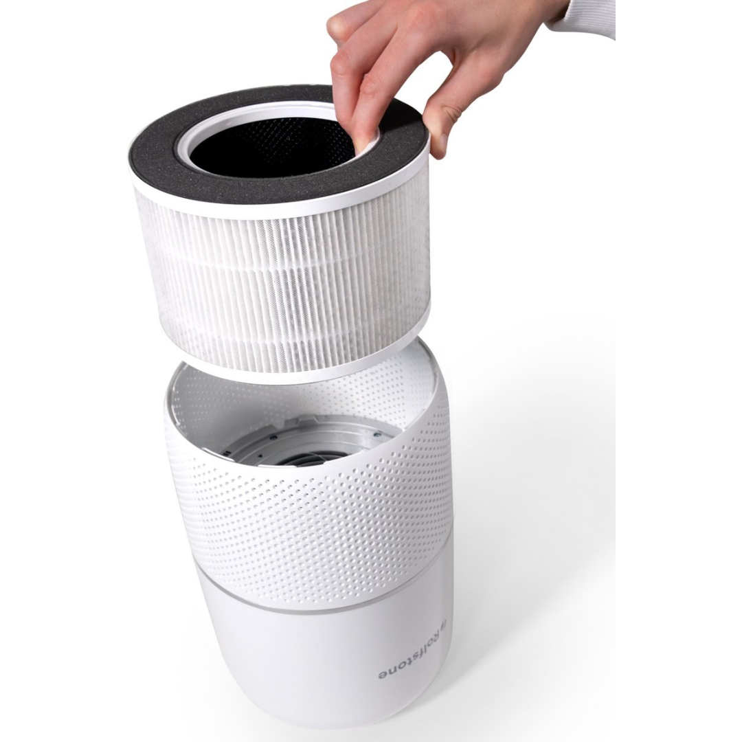 A hand replaces a round white air filter in a white air purifier.