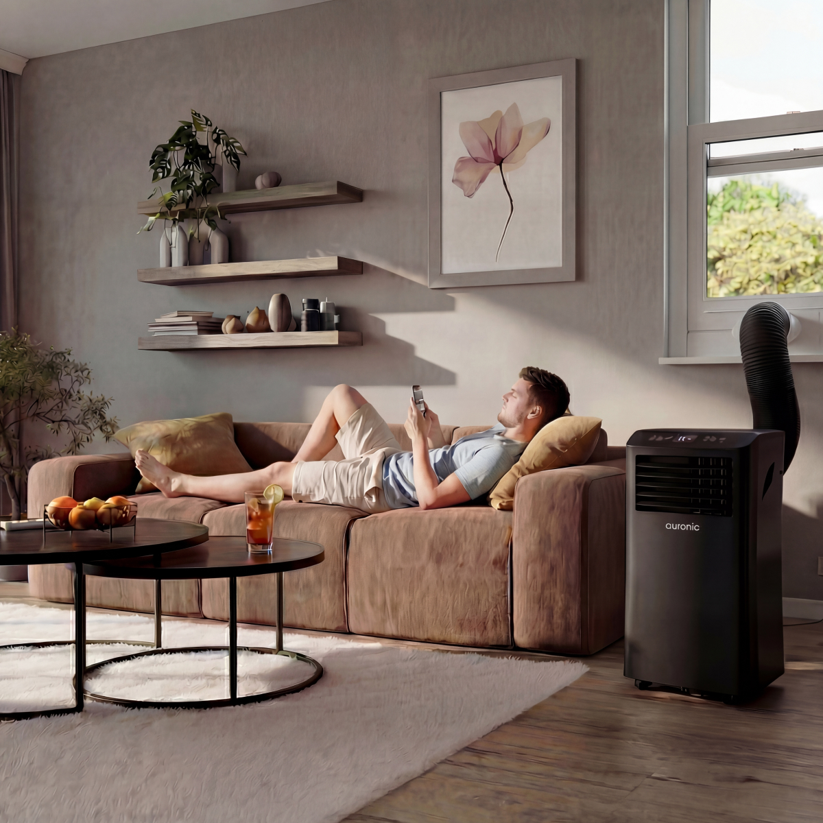 A man relaxes on a brown couch using his phone. A portable air conditioner is beside him.