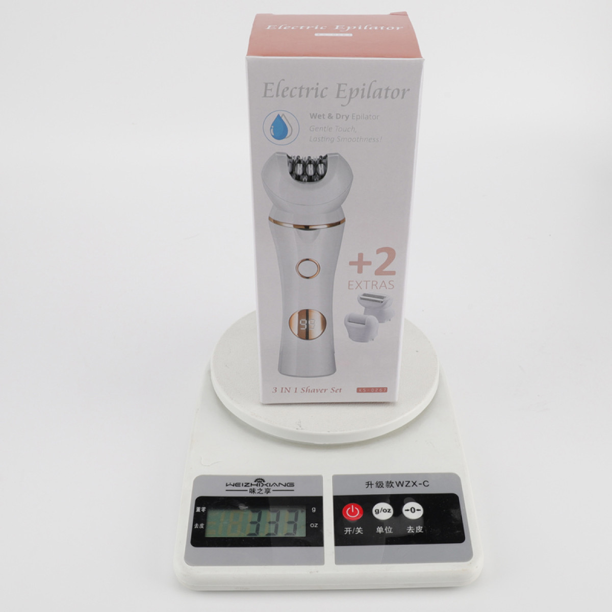 Weiße Verpackung für einen elektrischen Epilierer mit goldenen Akzenten auf einer Digitalwaage, die 333 anzeigt.