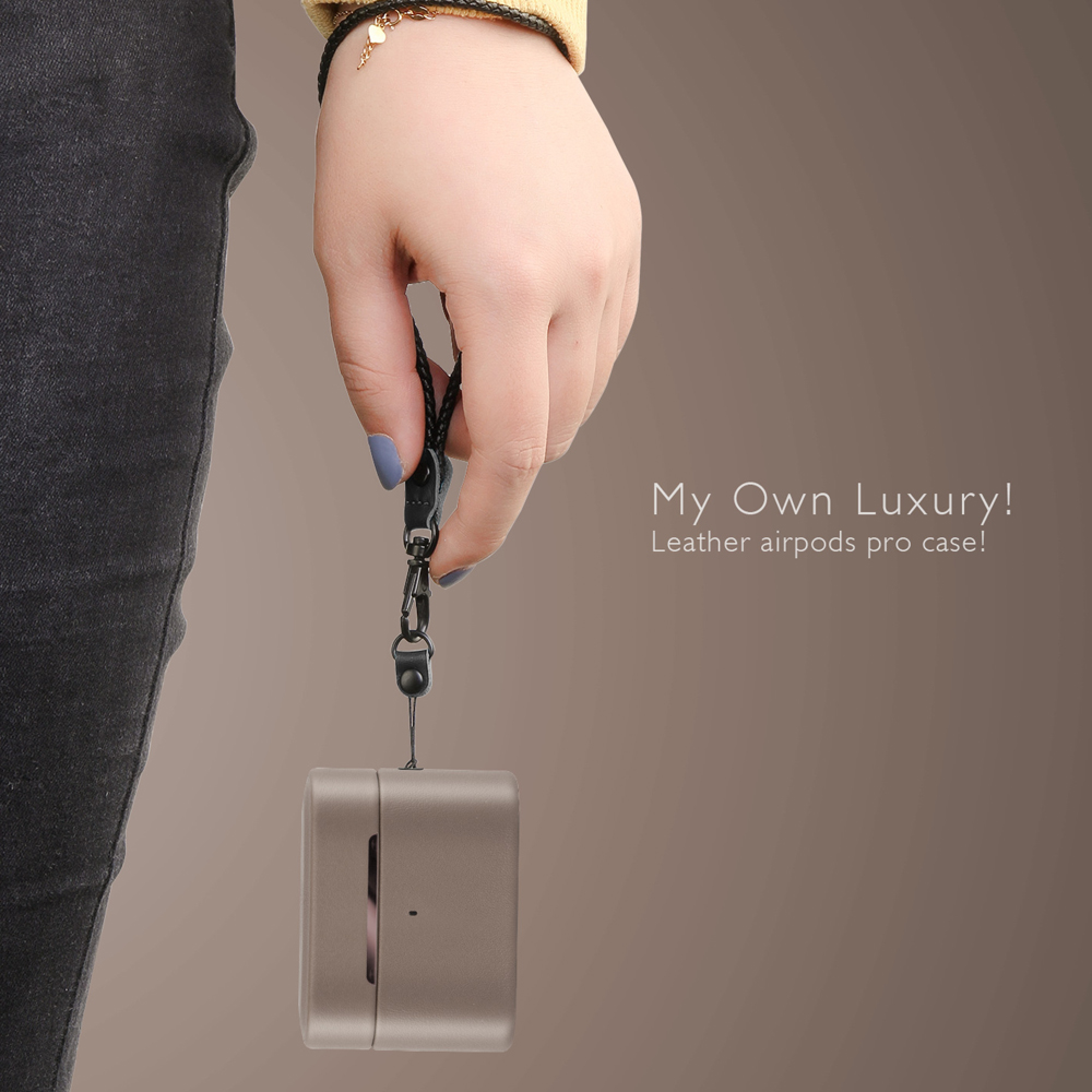 Eine Hand hält eine bronzefarbene AirPods Pro-Hülle an einer Schnur. Dunkle Jeans.