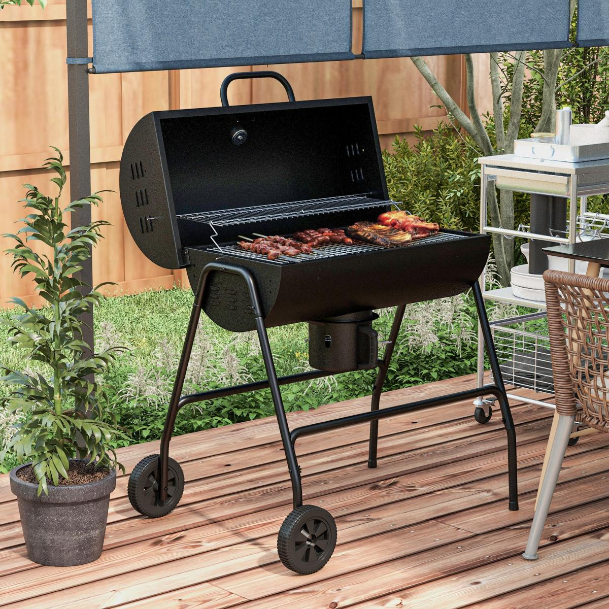 Ein schwarzer Grillwagen mit Fleisch und Spießen auf dem Rost, auf einem Holzdeck.