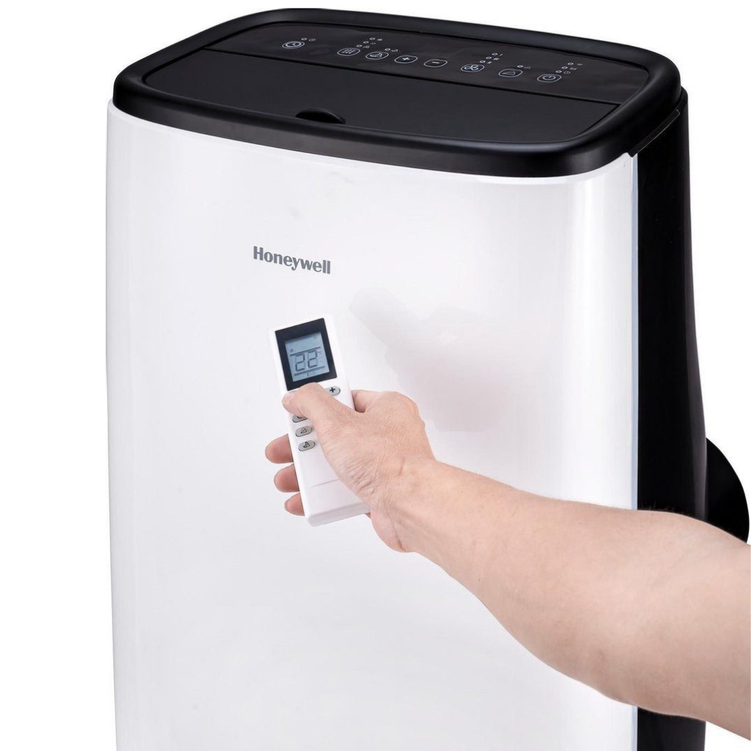 Eine Hand hält eine weiße Fernbedienung vor einem weißen Honeywell-Luftkühler.