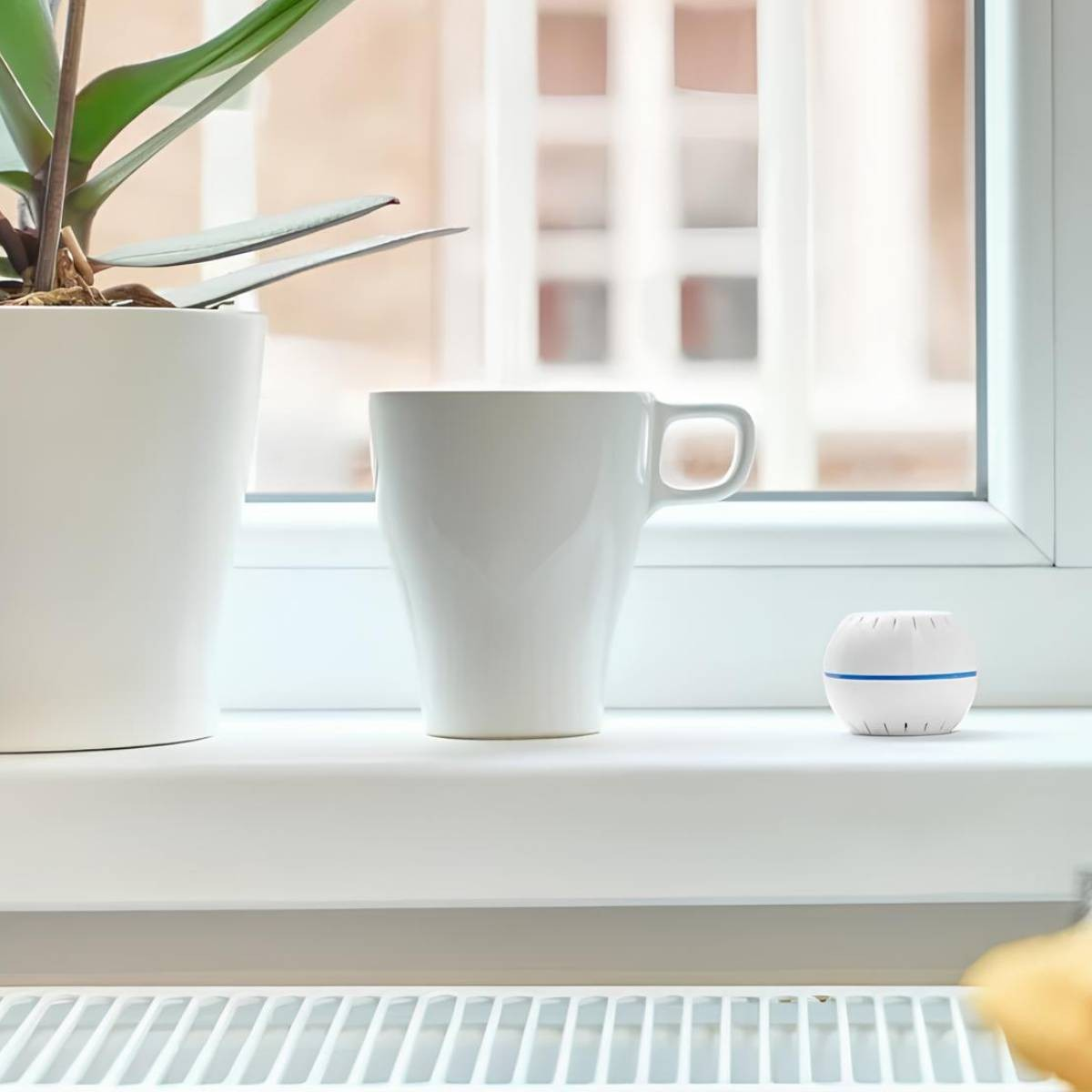 Una tazza bianca, una pianta in vaso e un piccolo dispositivo bianco sul davanzale.