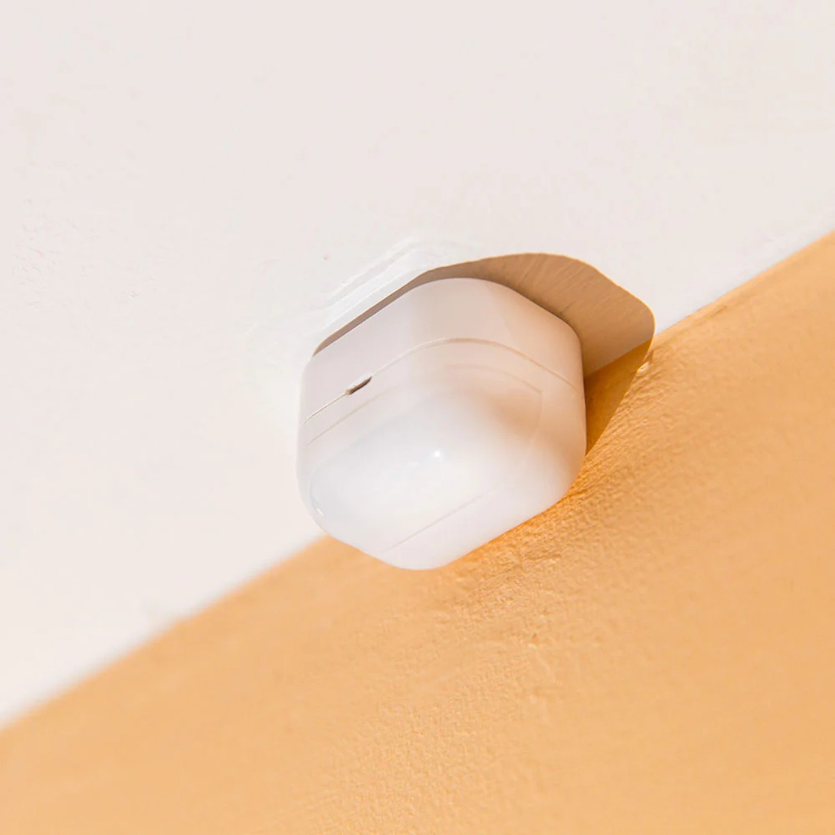 Sensore di movimento bianco attaccato a soffitto bianco e parete arancione.