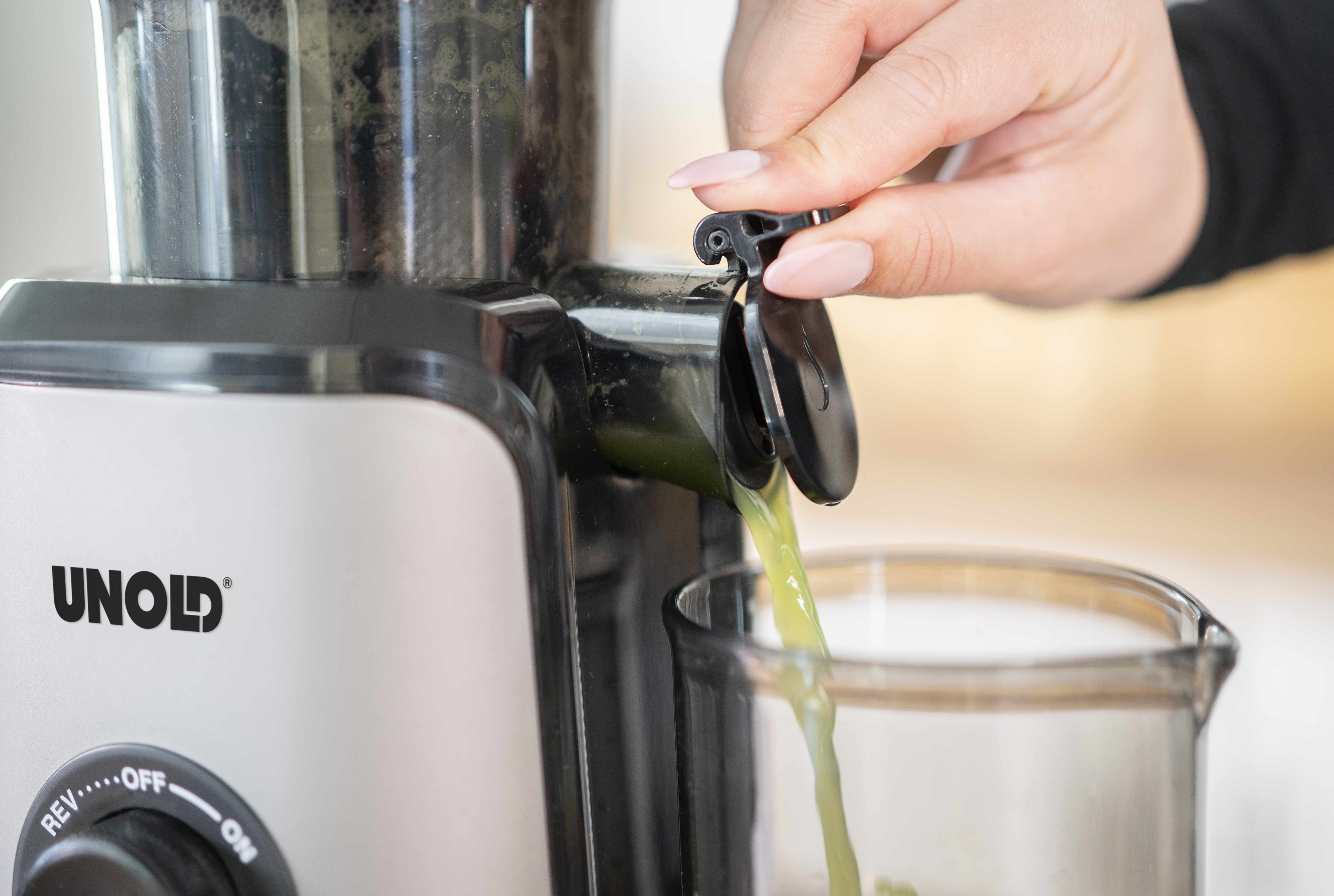 Una mano con smalto chiude il beccuccio di una centrifuga mentre il succo scorre in un bicchiere.