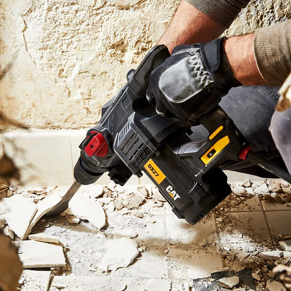 Person mit Schutzhandschuhen benutzt einen schwarzen Bohrhammer mit gelben Akzenten.