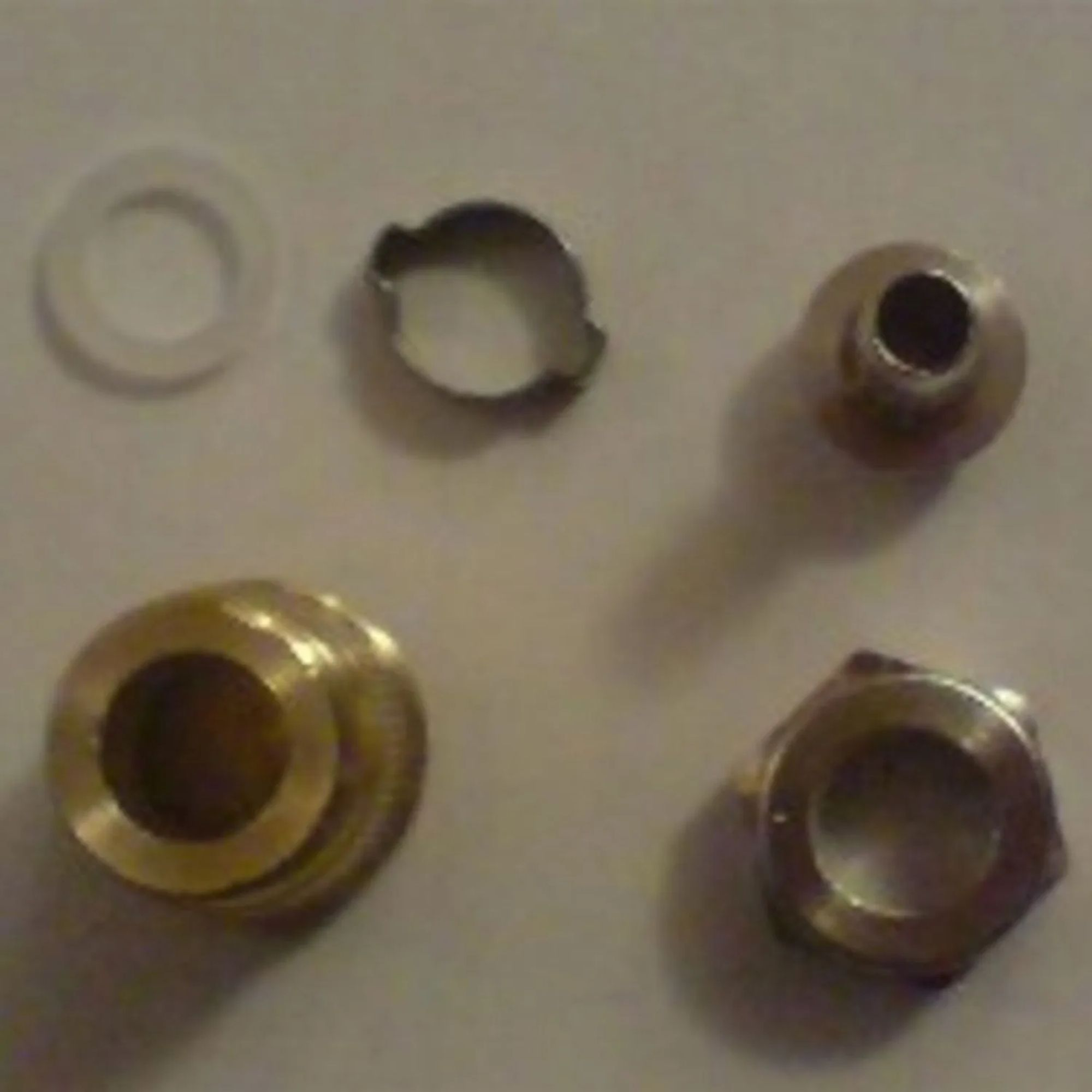 Quatre petites pièces métalliques et une rondelle blanche sur fond clair.