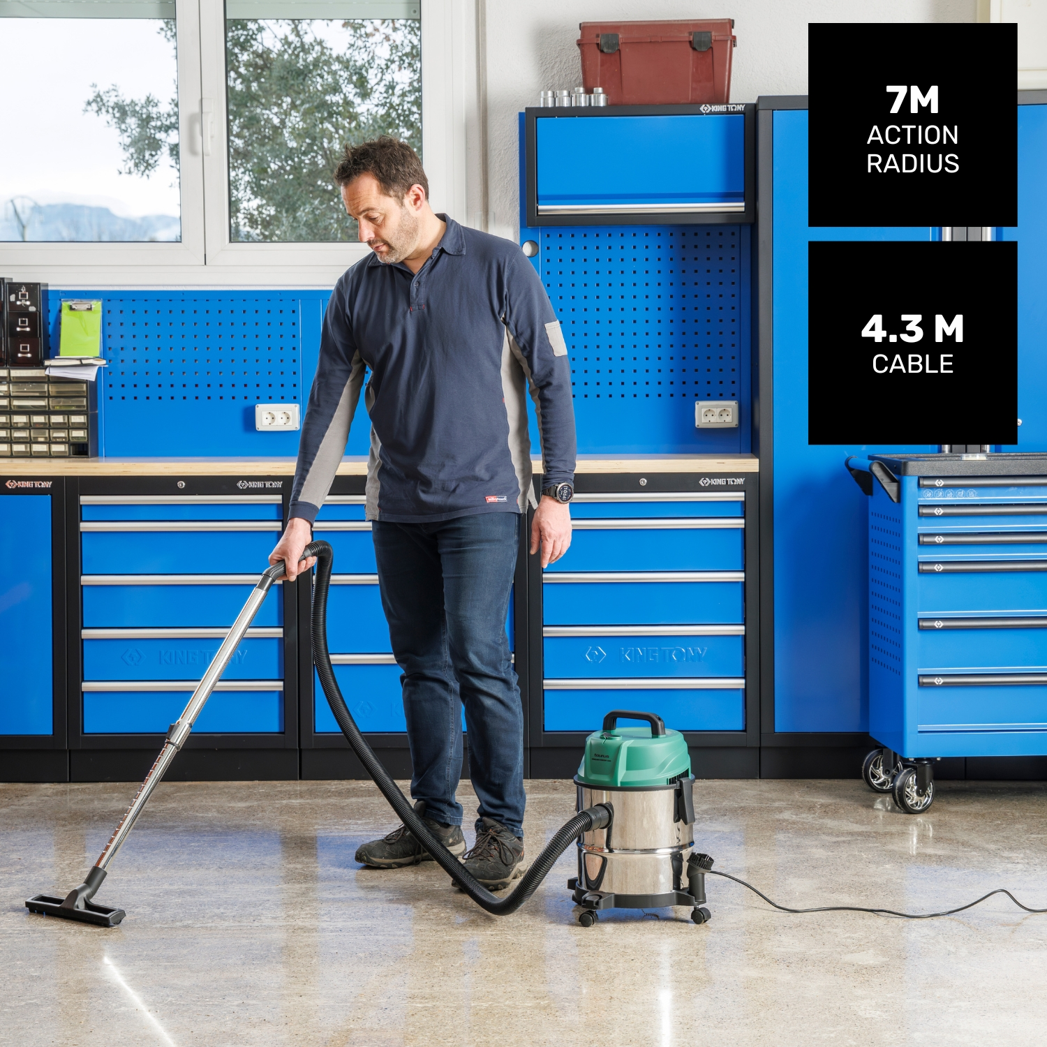 Hombre aspirando suelo de taller con aspiradora industrial; armarios azules al fondo.