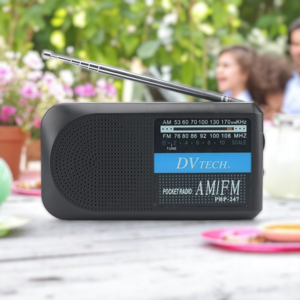 Una radio de bolsillo AM/FM negra con la antena extendida, sobre una mesa de madera.