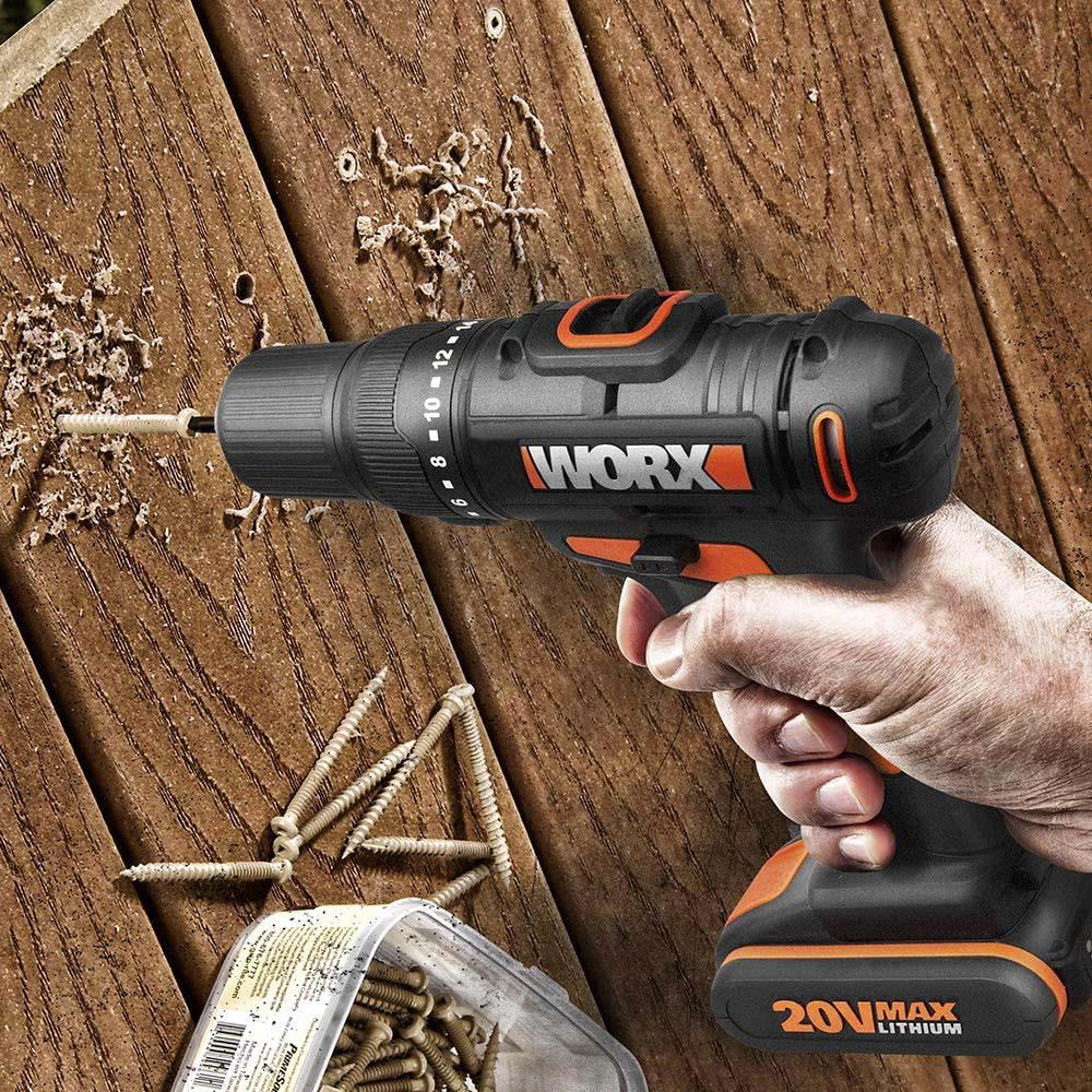 Una mano tiene un trapano Worx nero e arancione che fora il legno. Viti nelle vicinanze.