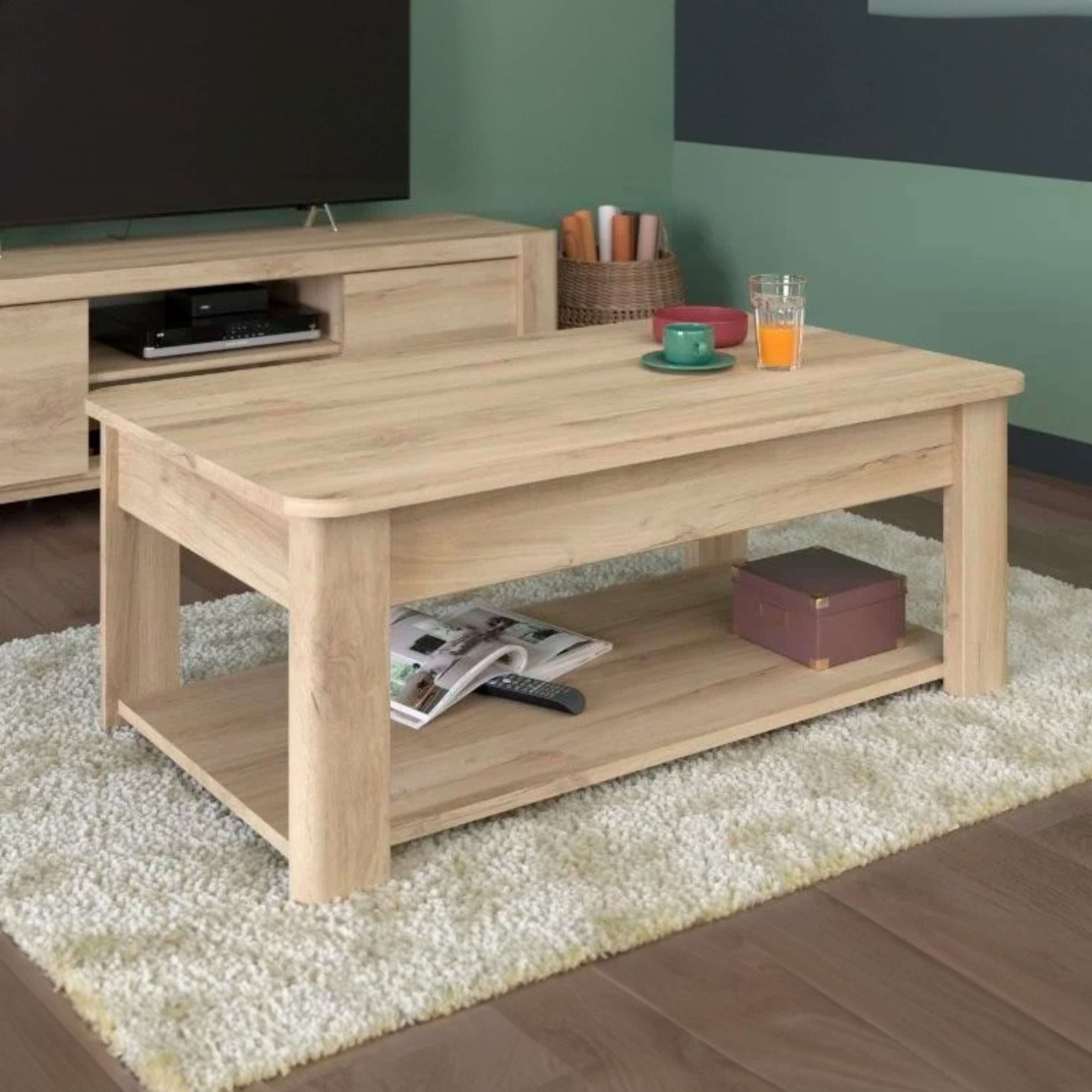 Una mesa de centro de madera clara con un estante debajo que sostiene revistas y un control remoto.
