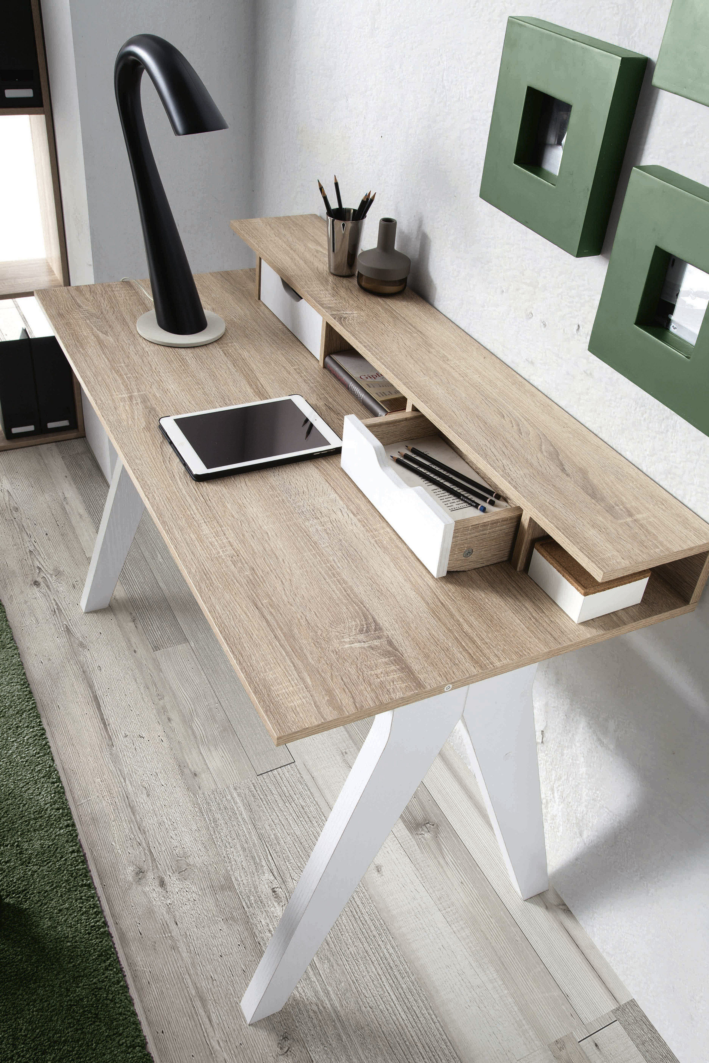 Escritorio moderno con tableta, lámpara, lápices y decoración de pared verde.