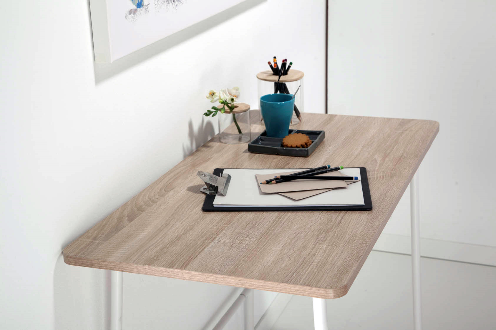 Escritorio de madera con portapapeles, bolígrafos, flor, galleta y taza azul.