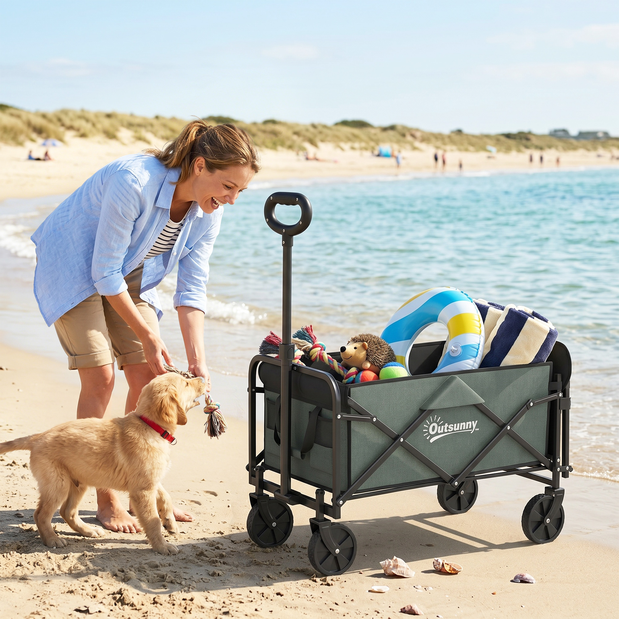 Una mujer y un perro juegan en la playa con un carrito lleno de artículos de playa.