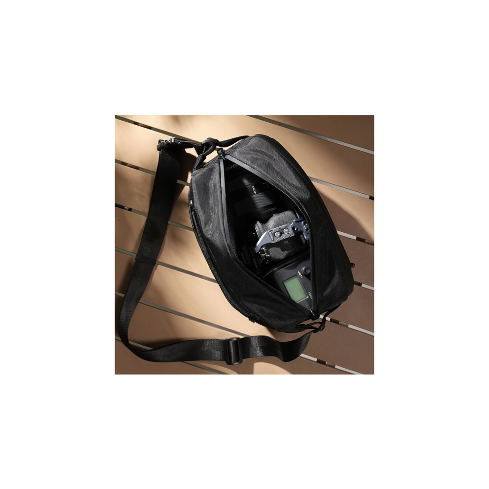 A black camera bag lies open on a wooden surface, revealing a camera and flash inside.