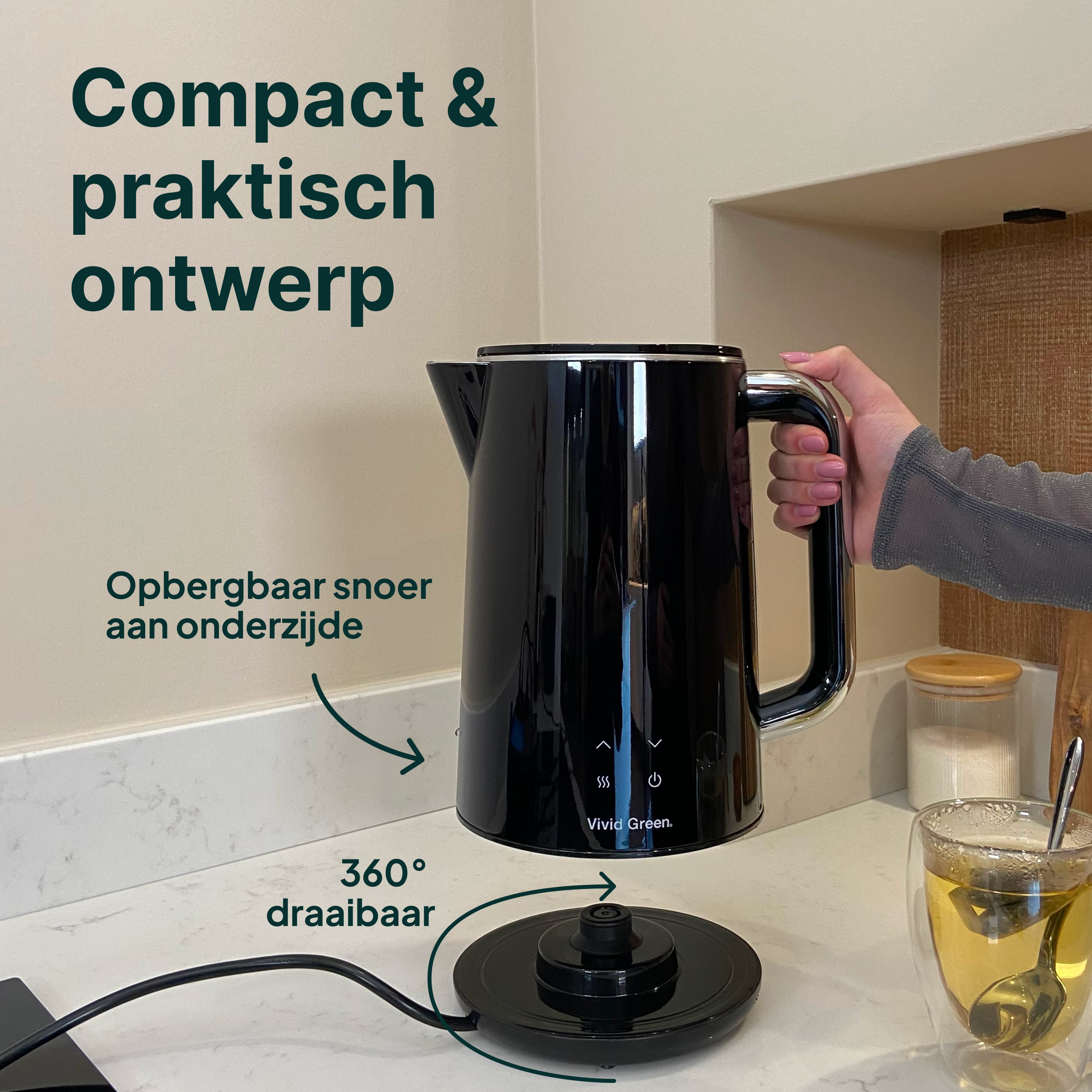 Zwarte waterkoker op aanrecht, hand pakt hem. Naast een glas thee.