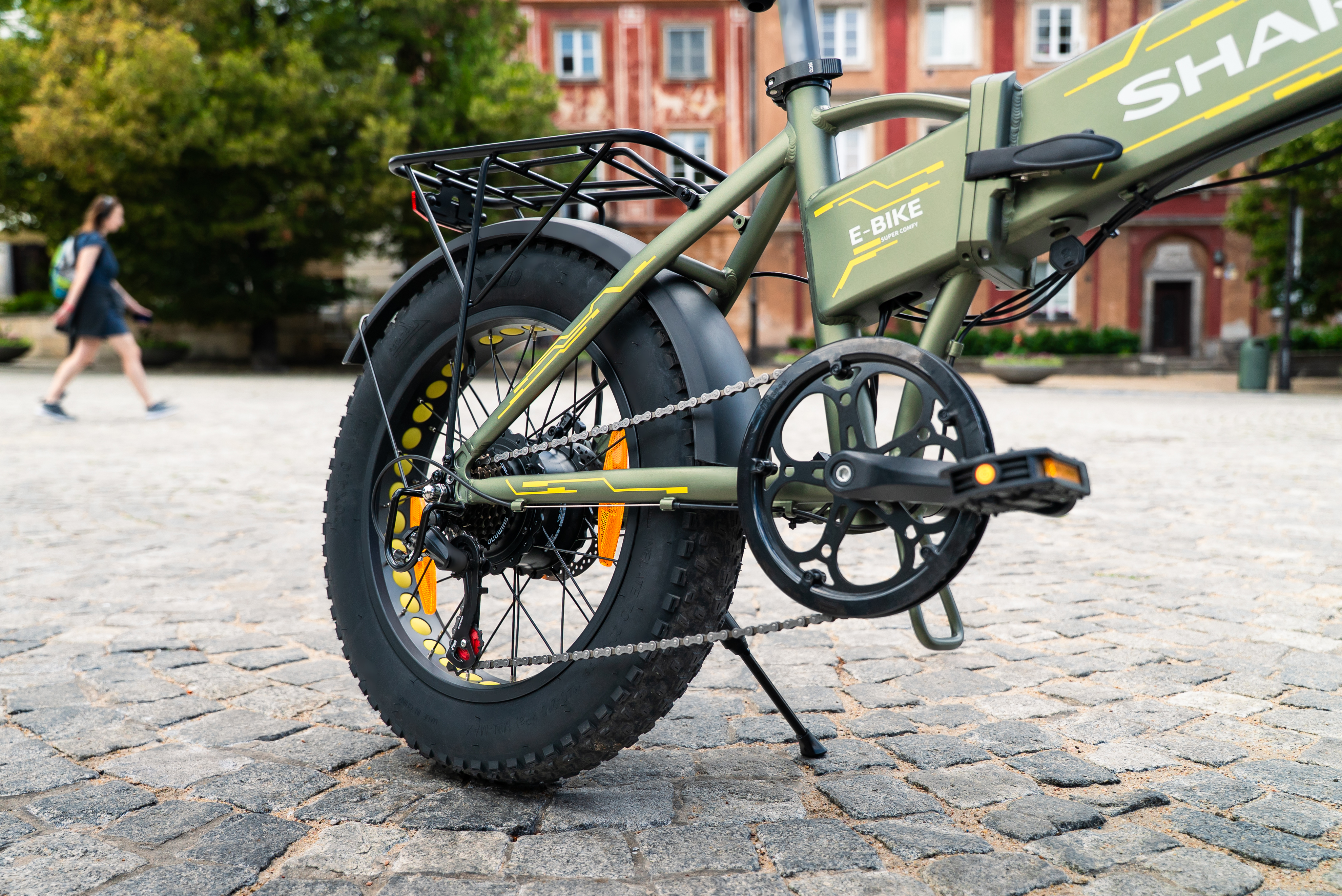 Grünes E-Bike mit fetten Reifen auf Kopfsteinpflaster, Gebäude im Hintergrund.