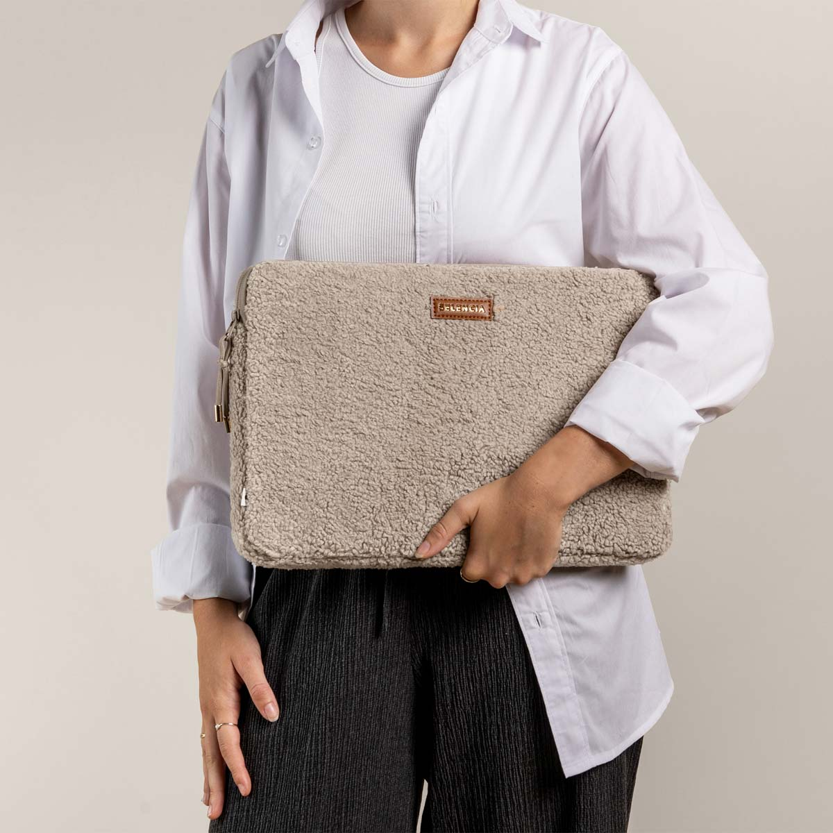 A person holds a beige teddy laptop bag with a brown logo.