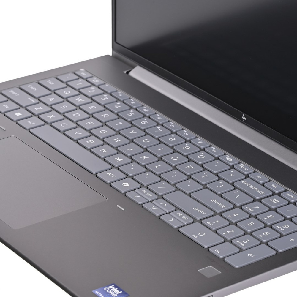 Szary laptop z podświetlaną klawiaturą i touchpadem. Widok z bliska.