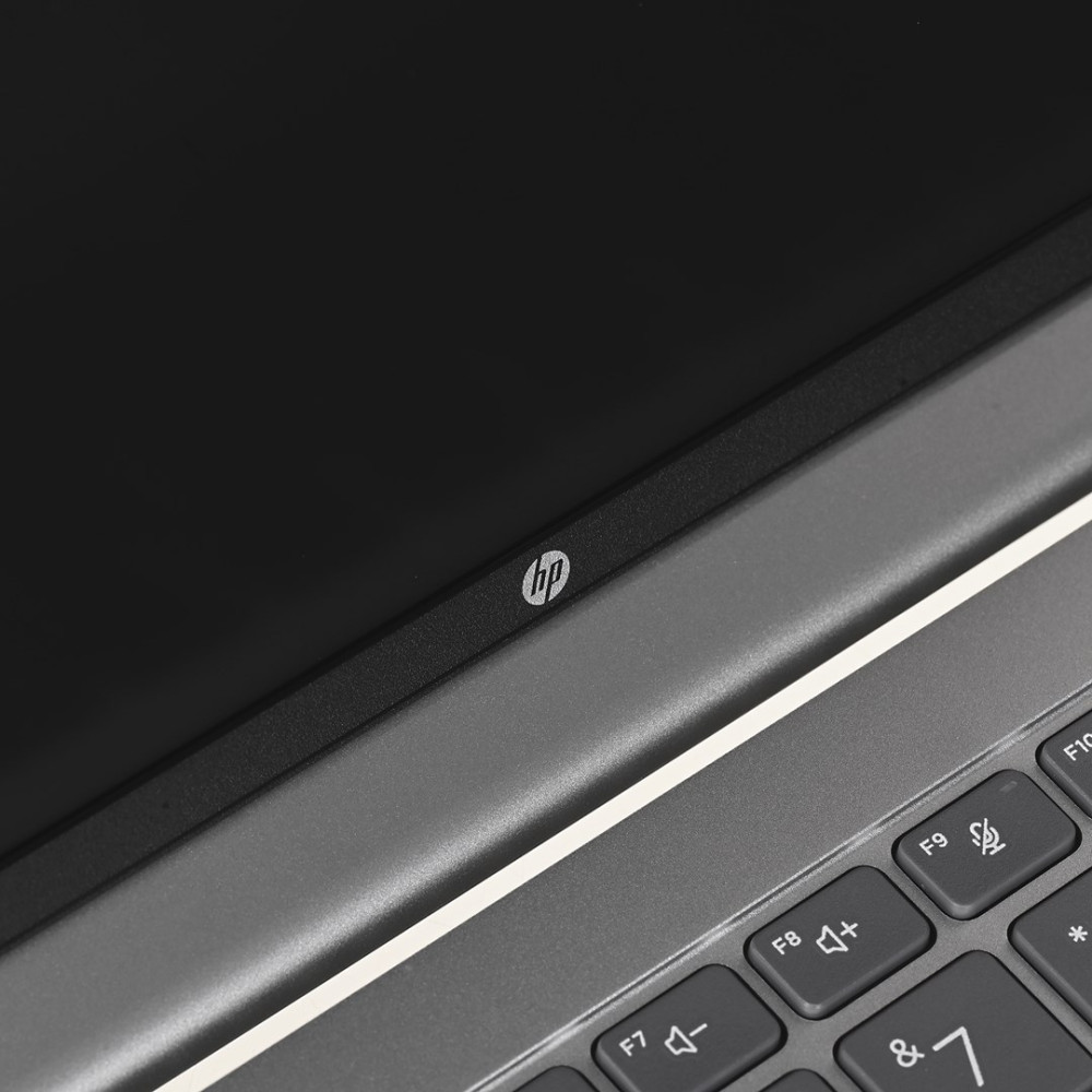 Zbliżenie logo HP na ciemnej ramce ekranu laptopa i klawiaturze.