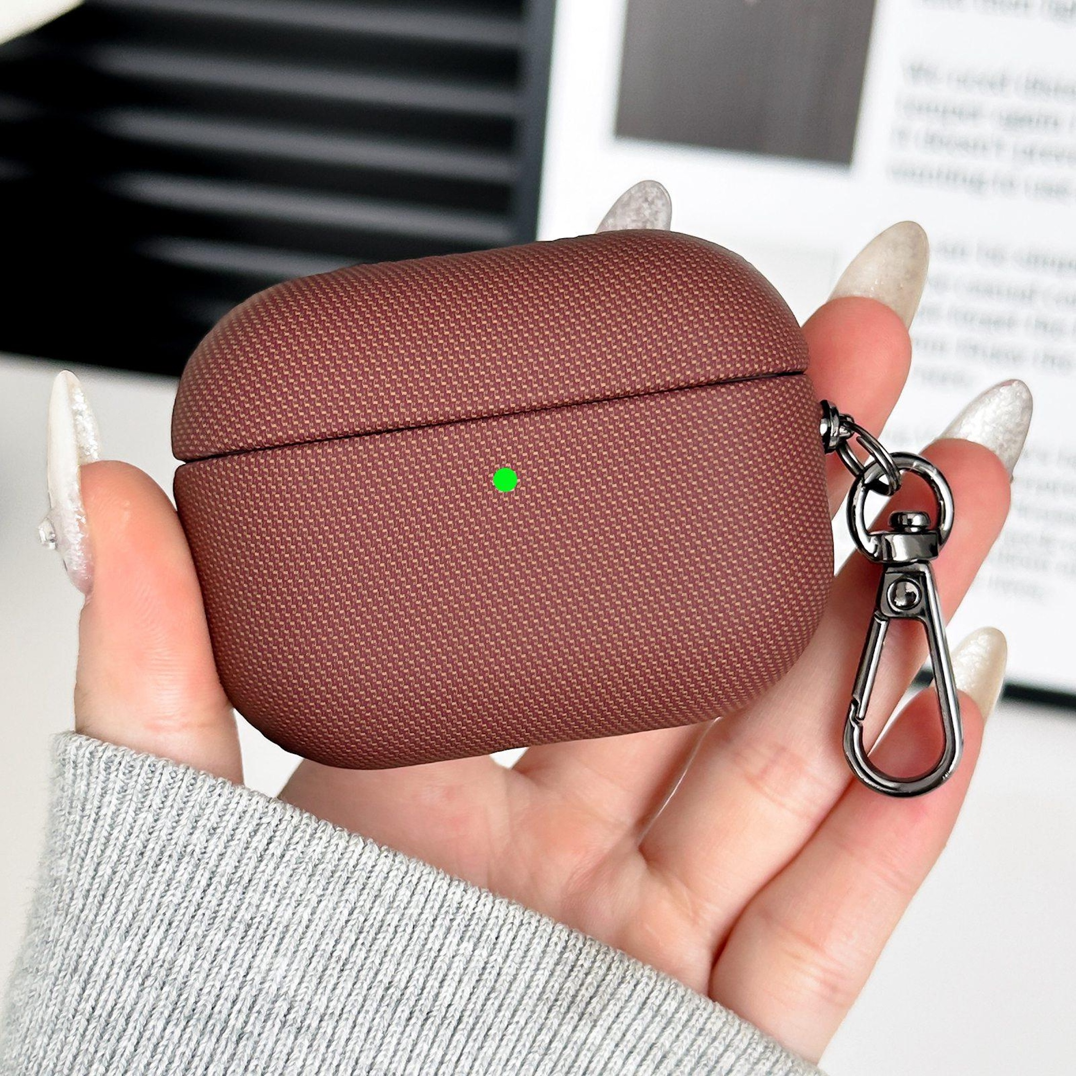 Funda marrón con clip de mosquetón, sostenida por una mano con esmalte de uñas.