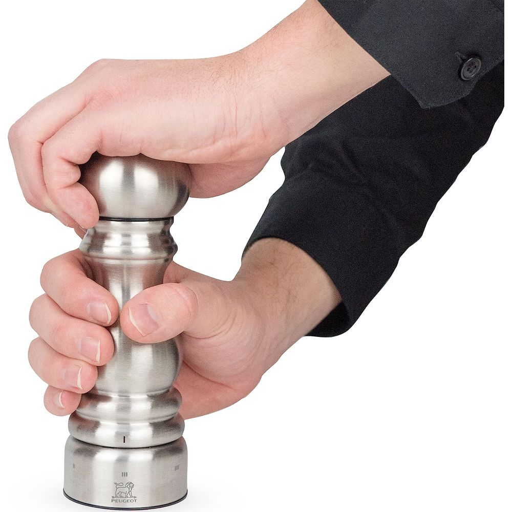 Eine Person dreht eine Edelstahl-Pfeffermühle mit beiden Händen.