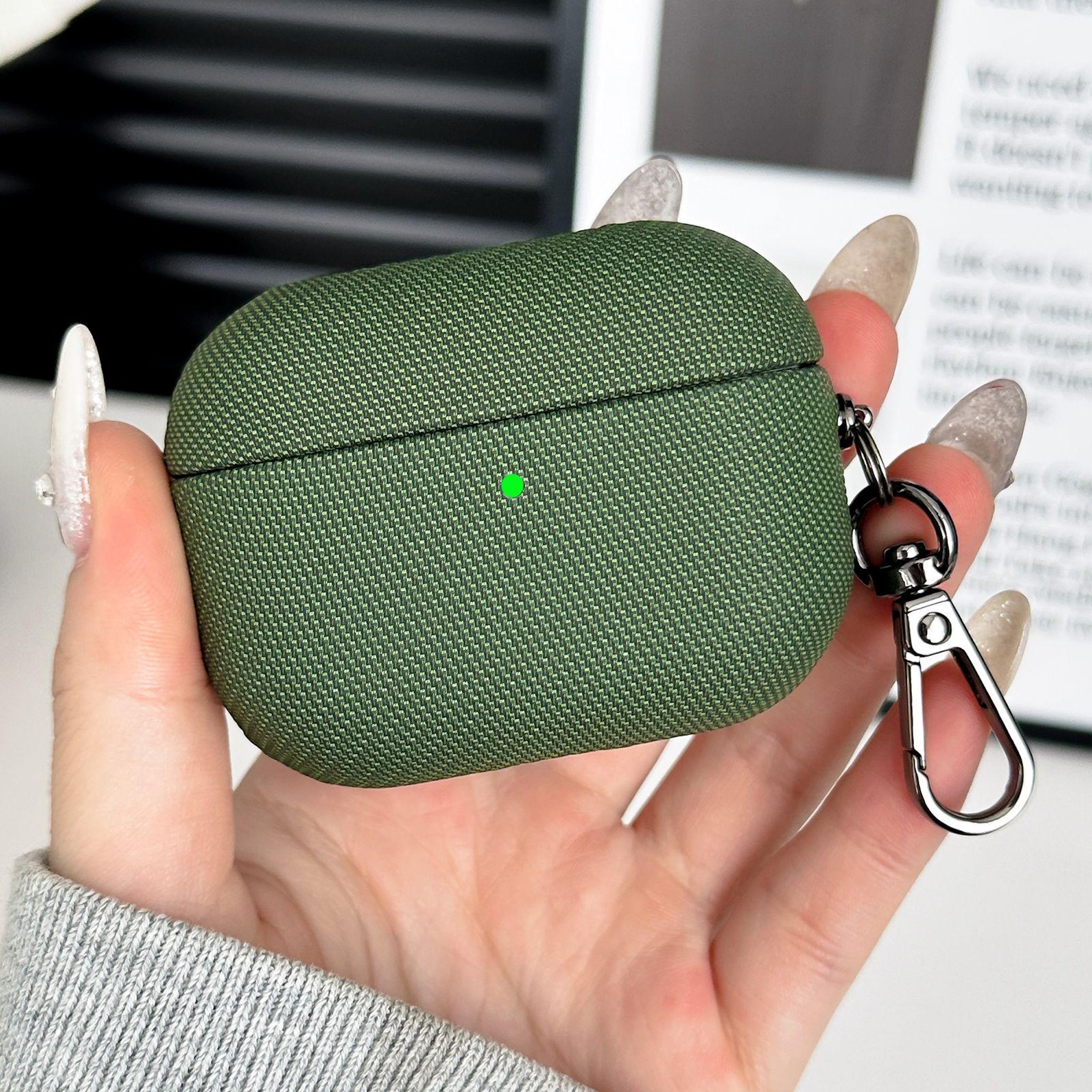 Funda verde para auriculares con mosquetón en la mano, pequeño punto verde en la funda.