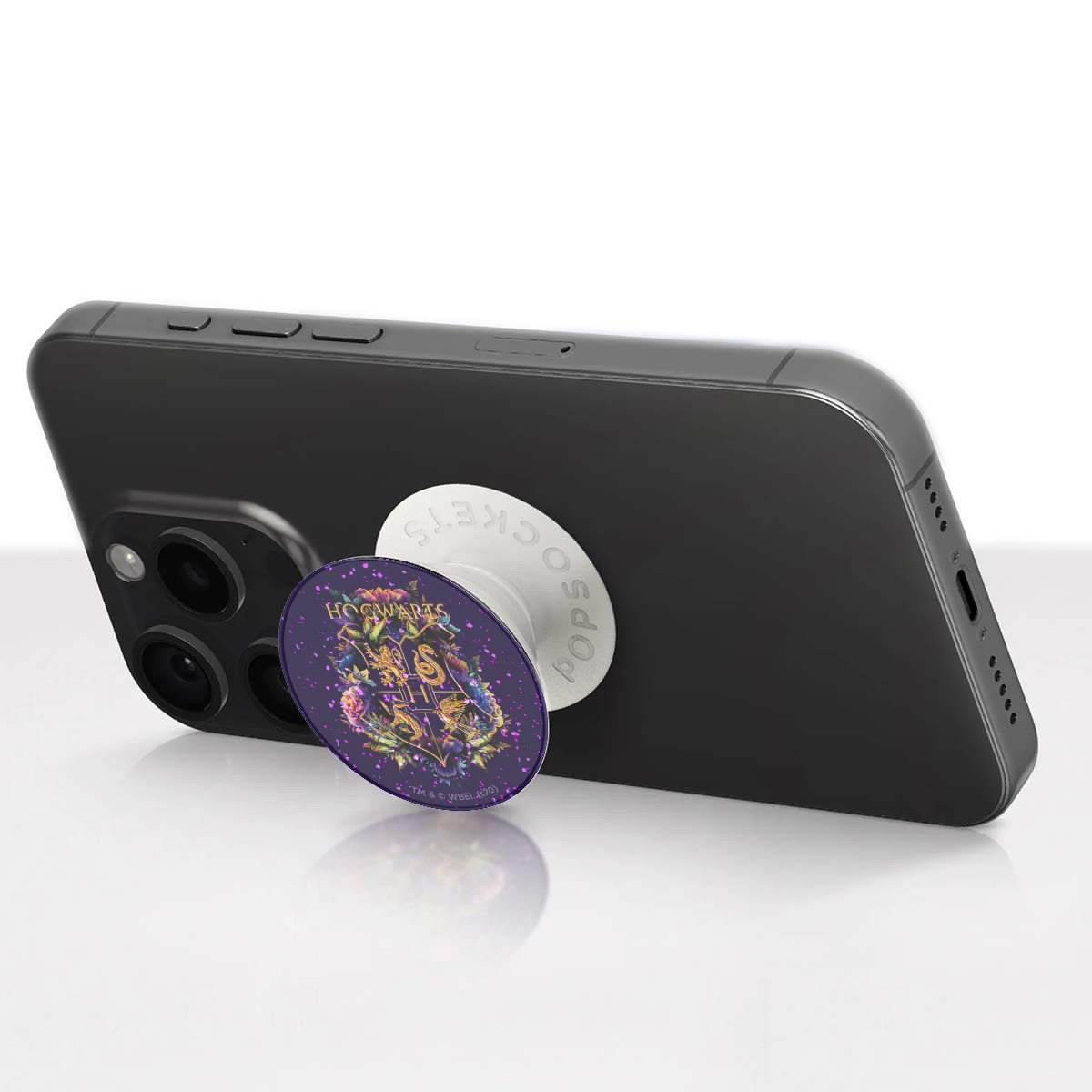 Un PopSocket con el logo de Hogwarts en un smartphone negro, fondo morado.