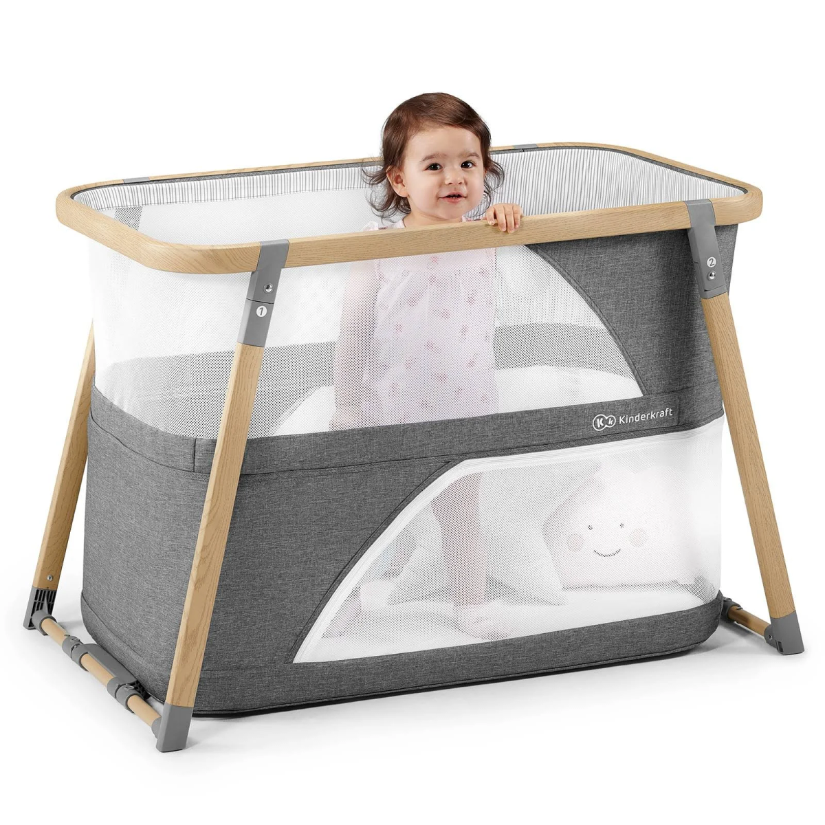 Ein Baby steht in einem Reisebett mit grauem Stoff und Holzrahmen.