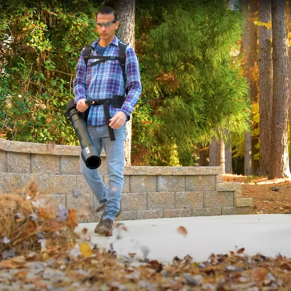 Uomo con soffiatore in autunno, che soffia via le foglie.