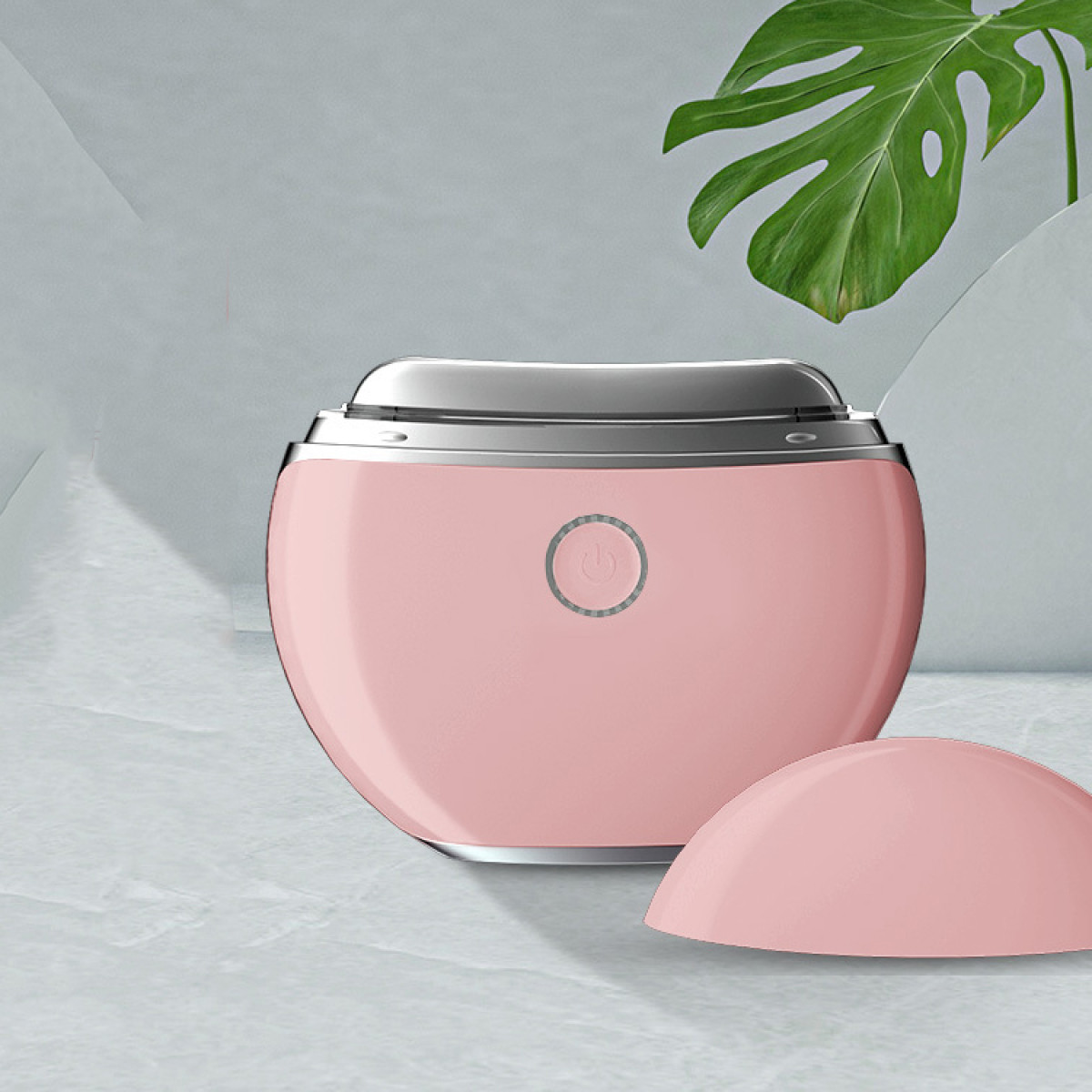 Un dispositivo ovale rosa con parte superiore argentata su superficie testurizzata. Grande foglia verde sullo sfondo.