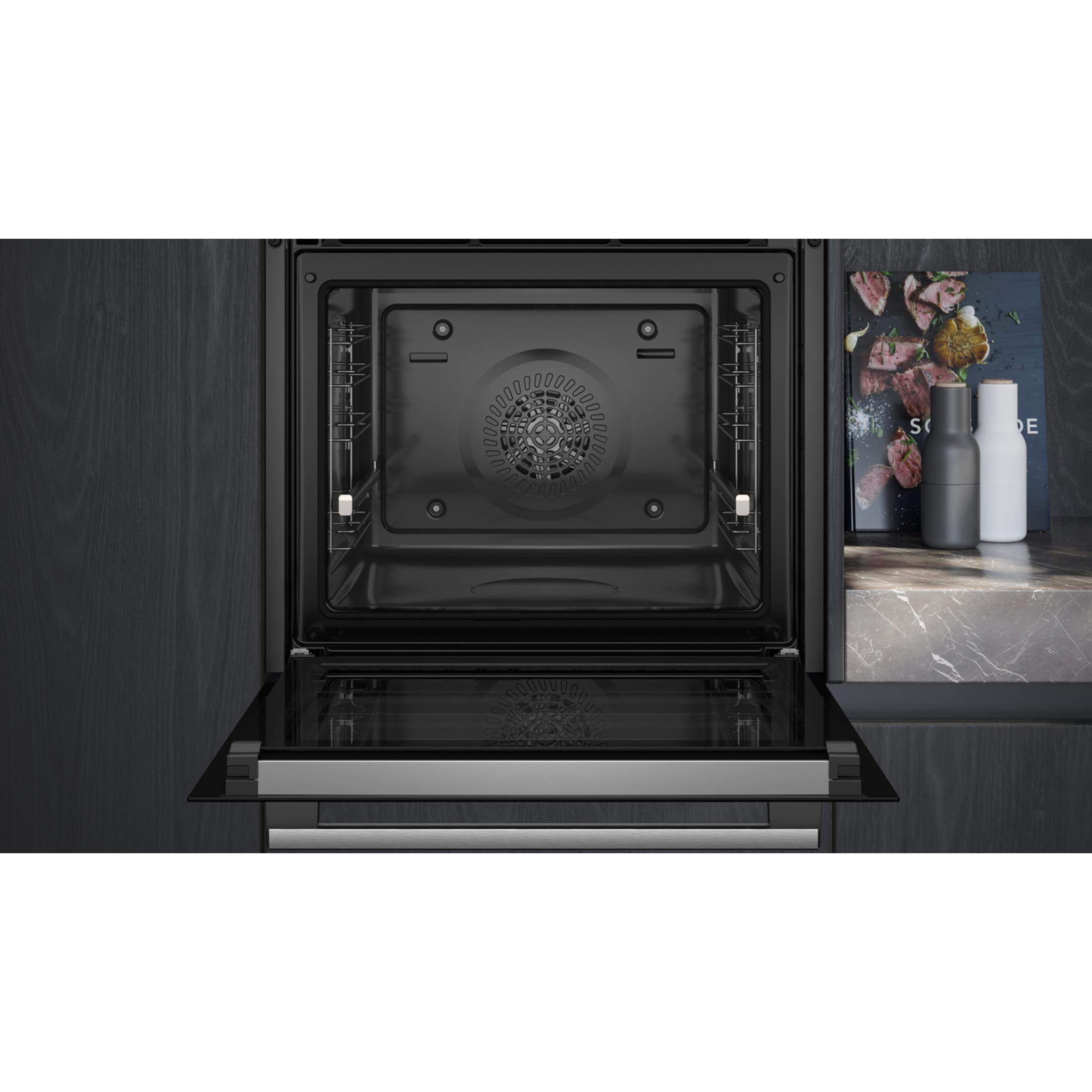 Un forno da incasso aperto con griglie argentate e griglia del ventilatore. Macina spezie accanto.